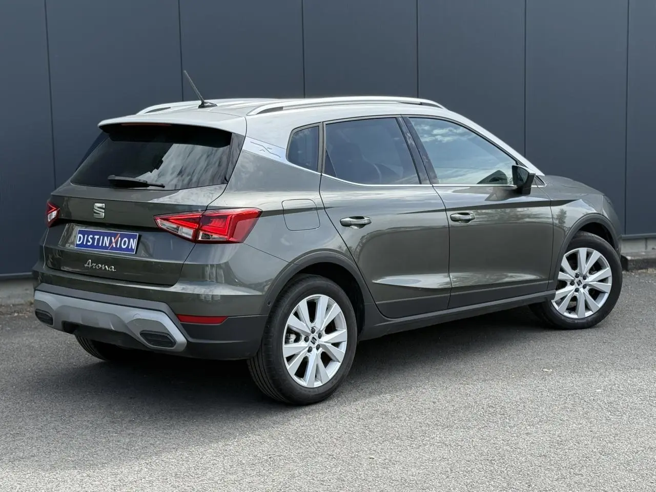 Vue 3/4 arrière droite du SEAT Arona gris Cliff avec toit blanc et jantes alliage 17 pouces sur fond urbain.