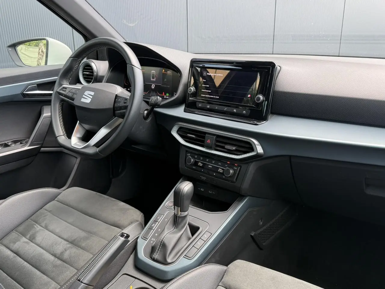 Vue intérieure côté conducteur du SEAT Arona 2025, mettant en valeur le volant, l'écran tactile et la sellerie en suédine noire.