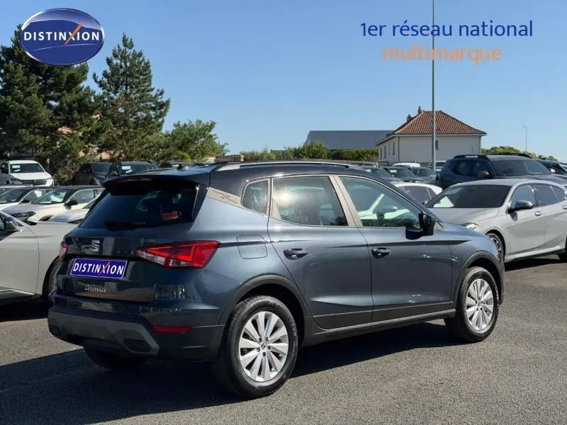 Vue 3/4 arrière droite d’un SEAT Arona gris magnétique métal avec toit noir, stationné en extérieur sur un parking.