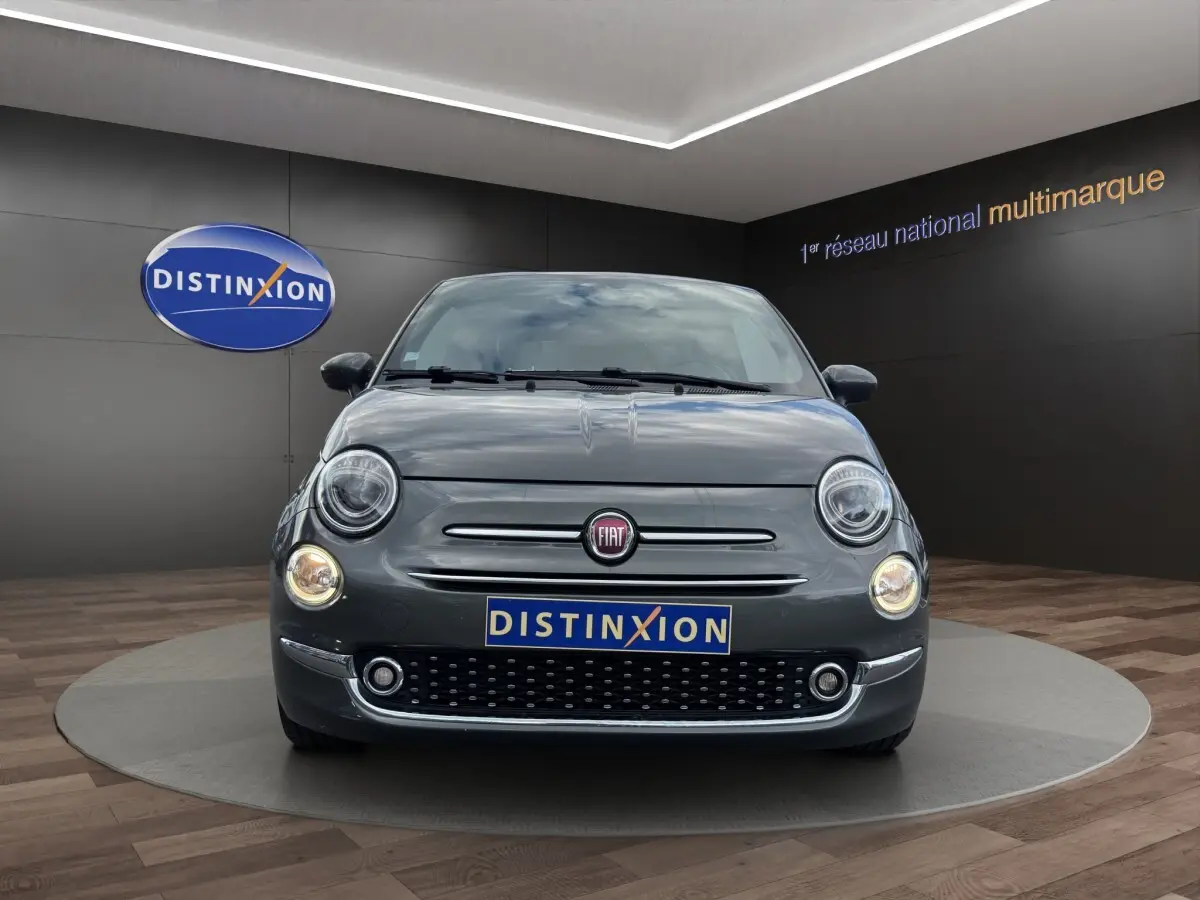 Vue avant de la Fiat 500 gris foncé avec phares ronds allumés et calandre chromée dans un showroom.