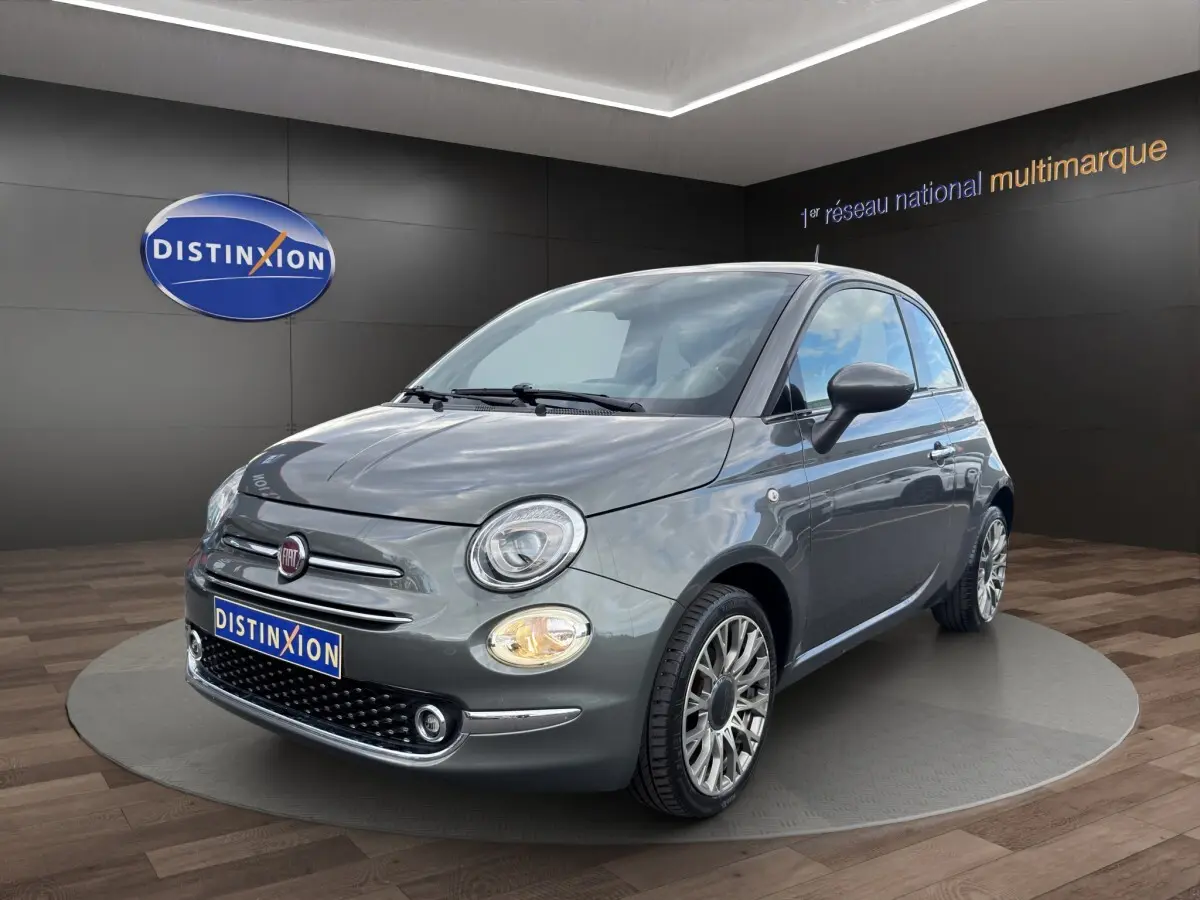 Fiat 500 gris foncé vue 3/4 avant droit, avec phares ronds et jantes alliage multibranches visibles.