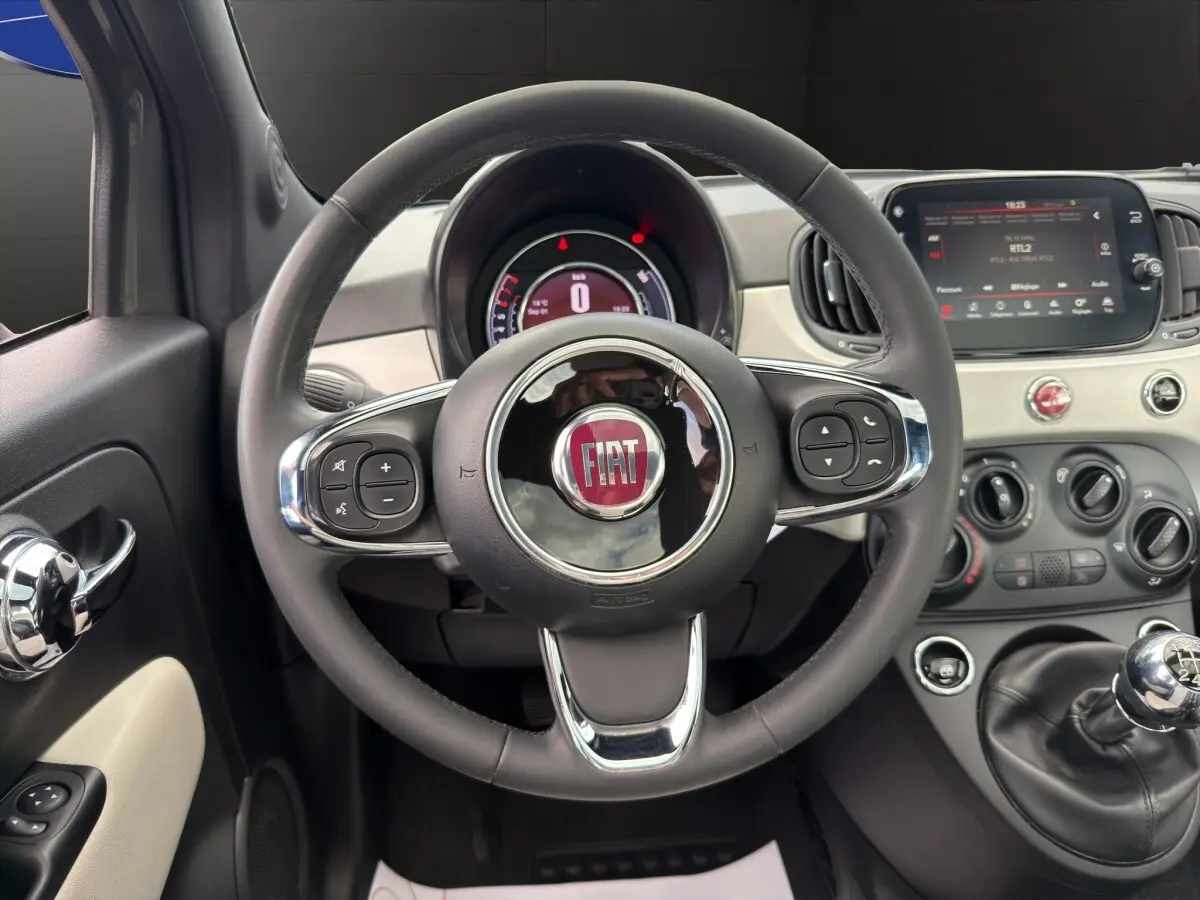 Vue intérieure centrée sur le volant cuir multifonctions d'une Fiat 500 2020 avec tableau de bord et écran tactile.