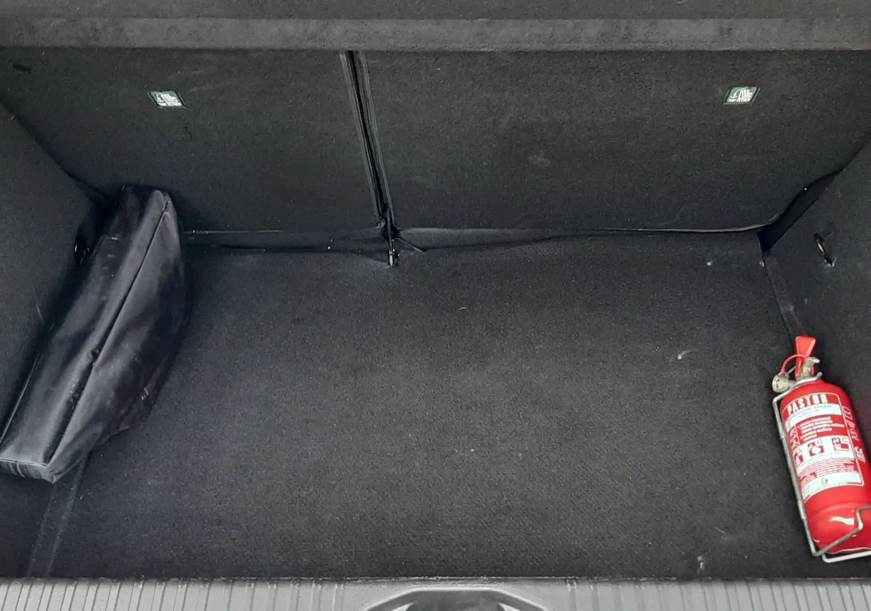 Coffre ouvert de la Renault Clio V gris schiste, montrant un extincteur rouge à droite et une trousse noire à gauche.