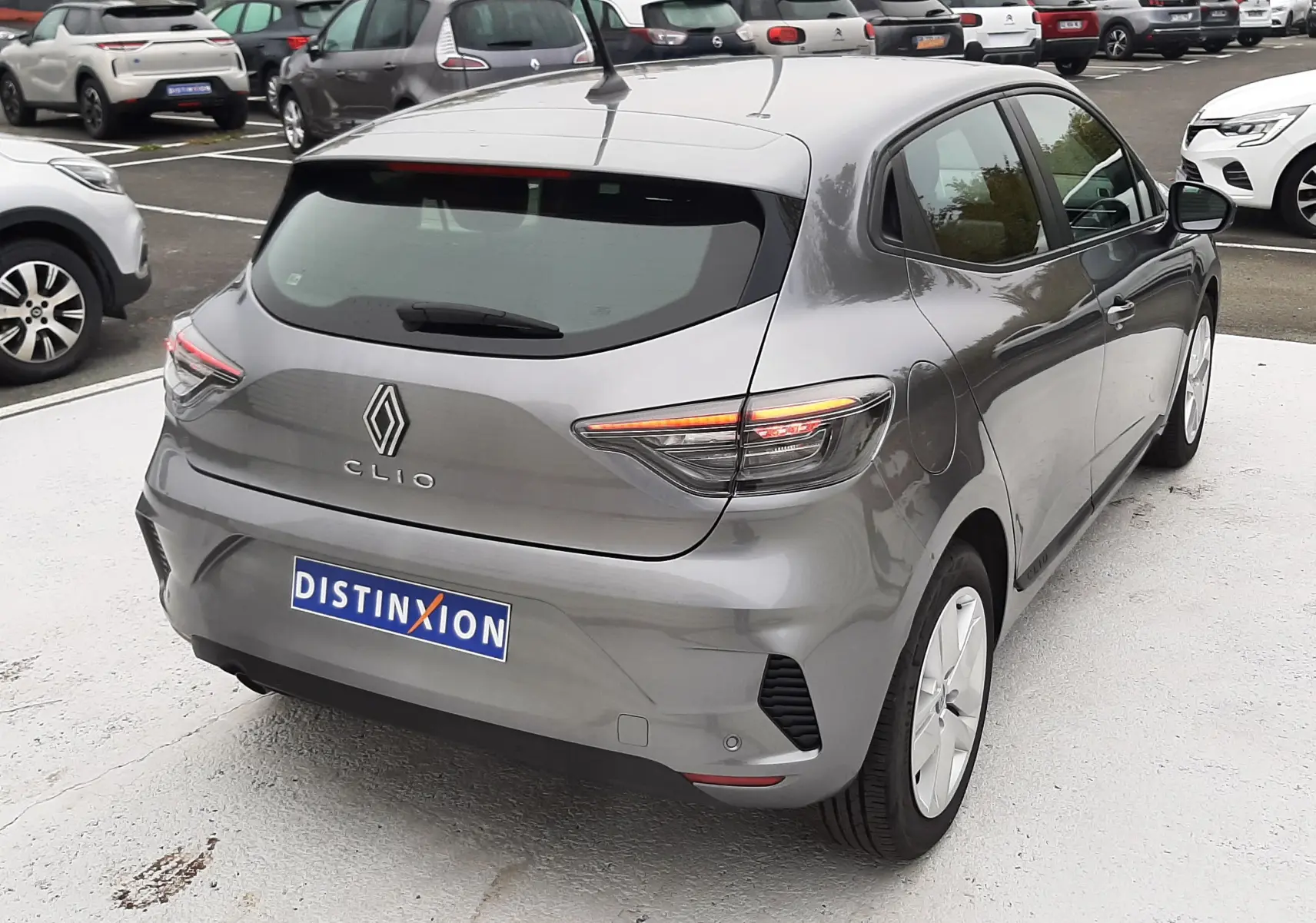 Vue 3/4 arrière droite d'une Renault Clio V TCE 90CH Evolution gris schiste avec feux arrière LED allumés sur parking.