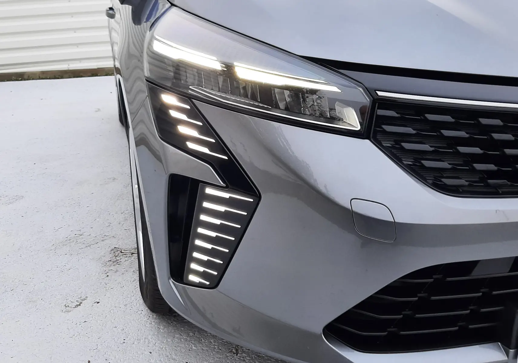 Gros plan sur l'avant droit d'une Renault Clio V gris schiste avec feux LED allumés et calandre noire.