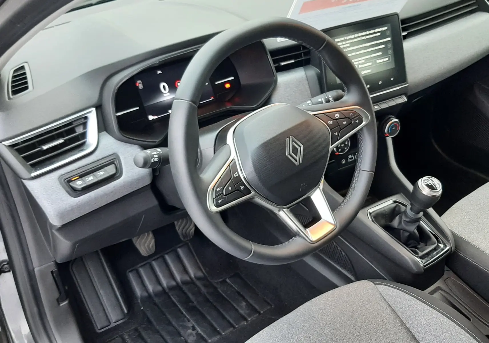 Intérieur de la Renault Clio V TCE 90CH Evolution 2025, vue côté conducteur sur volant, tableau de bord et levier de vitesses manuel.