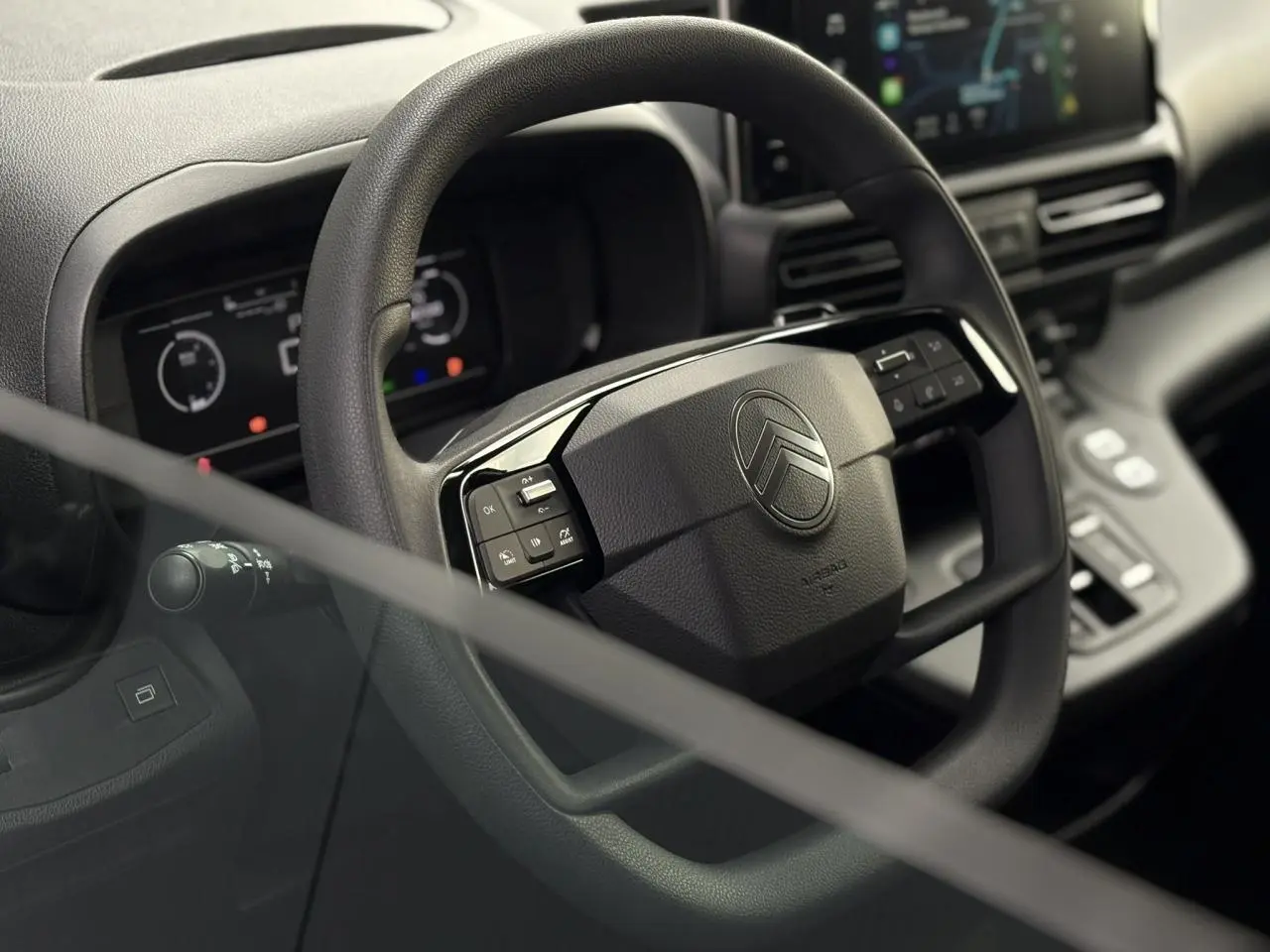 Vue rapprochée du volant multifonctions noir du Citroën Berlingo 2025 avec tableau de bord numérique en arrière-plan.
