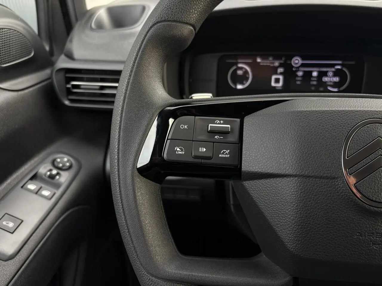 Gros plan sur le volant multifonctions noir du Citroën Berlingo 2025 avec commandes de régulateur et tableau de bord numérique.