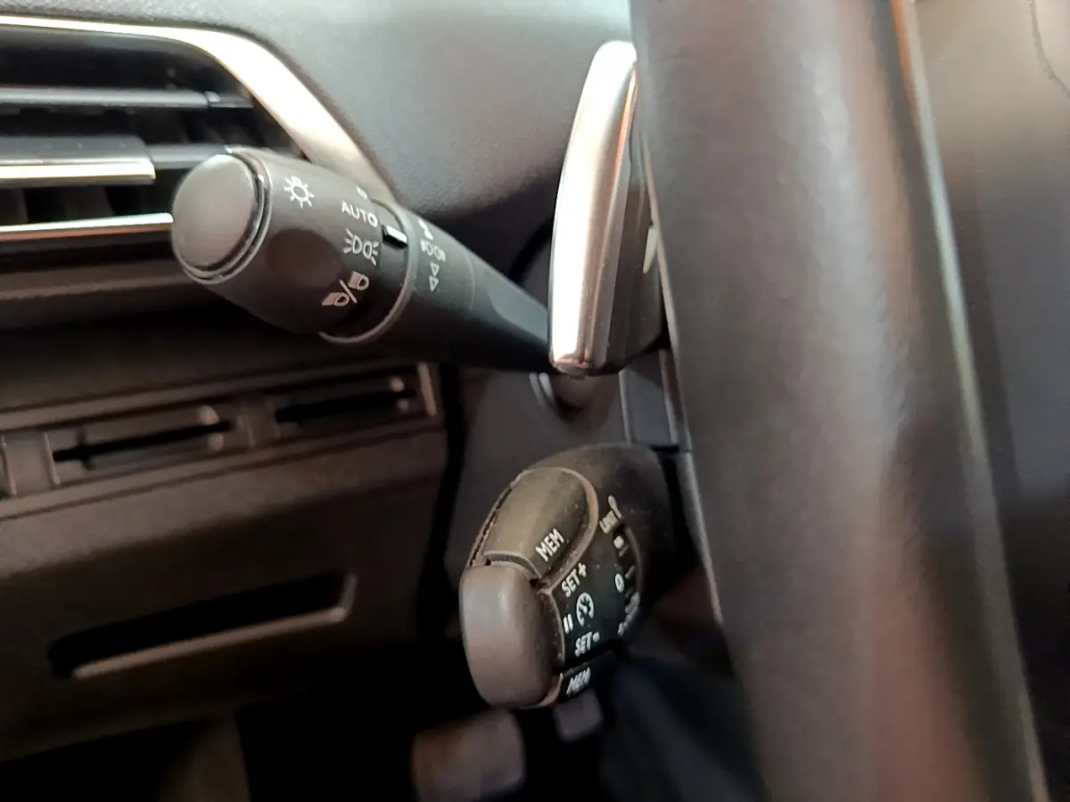 Gros plan sur commandes au volant côté gauche du Peugeot 3008 blanc, avec leviers de clignotants et régulateur de vitesse.