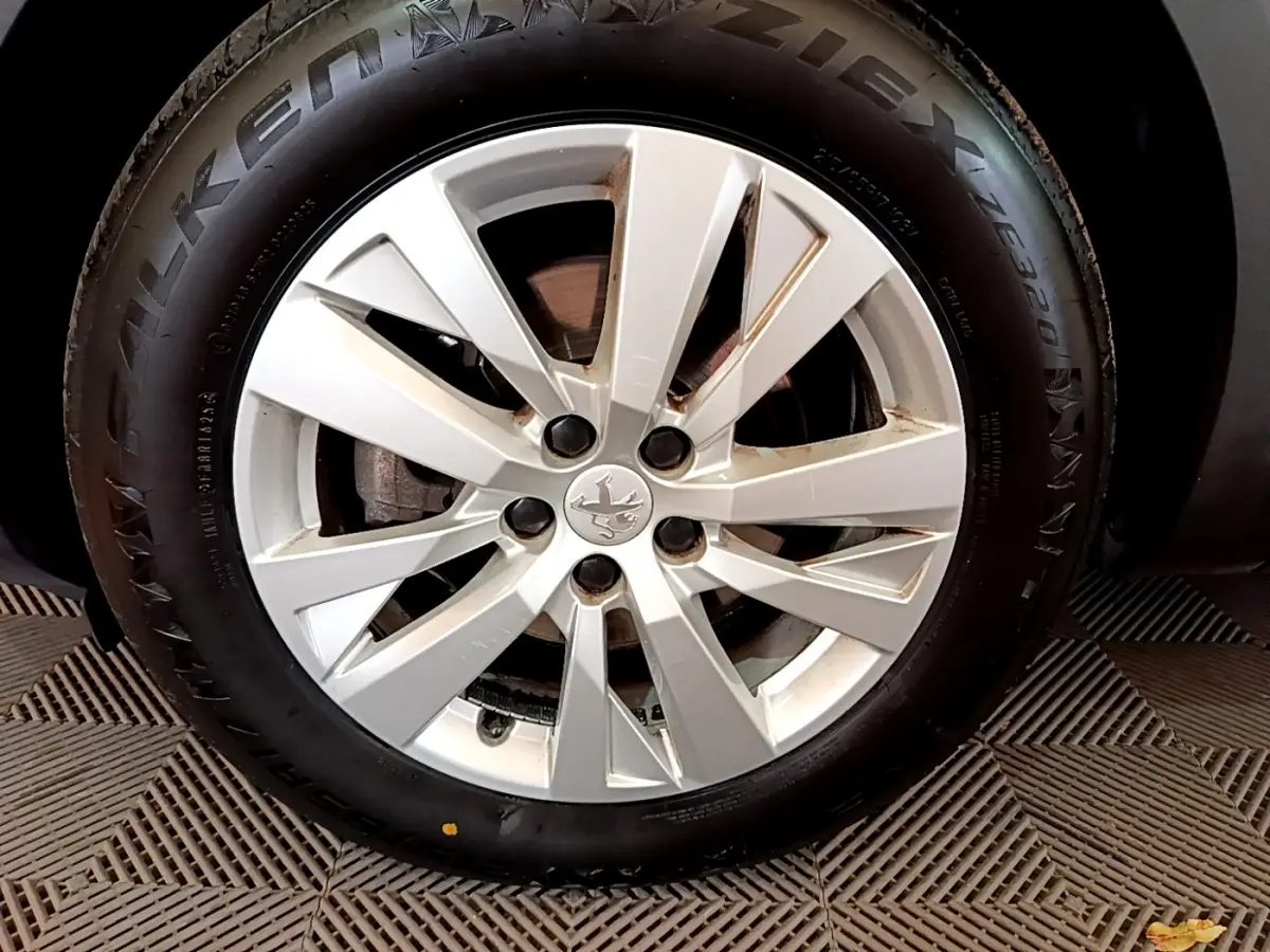 Gros plan sur la jante alliage argentée et pneu noir d'un Peugeot 3008 blanc, avec logo lion au centre.