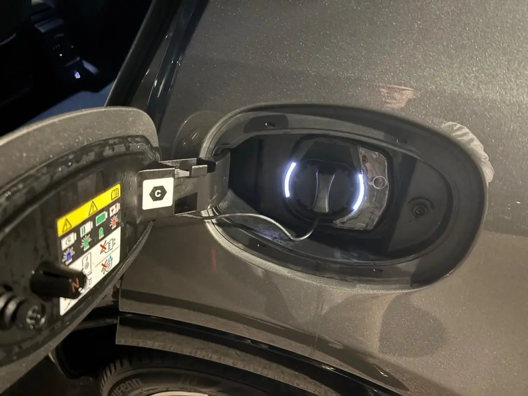 Détail de la trappe de recharge ouverte côté gauche sur Alfa Romeo Tonale gris 2023 avec câble de charge connecté.