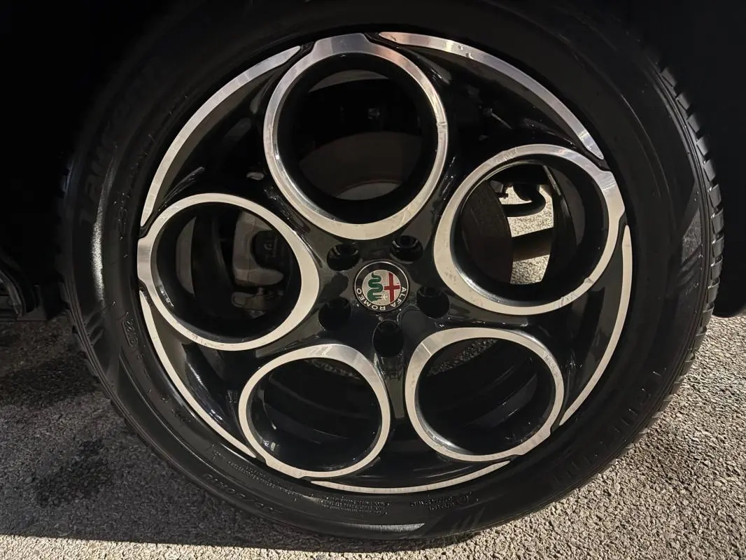 Gros plan sur la jante alliage noire et argentée de 18 pouces avec logo Alfa Romeo au centre, sur roue arrière.
