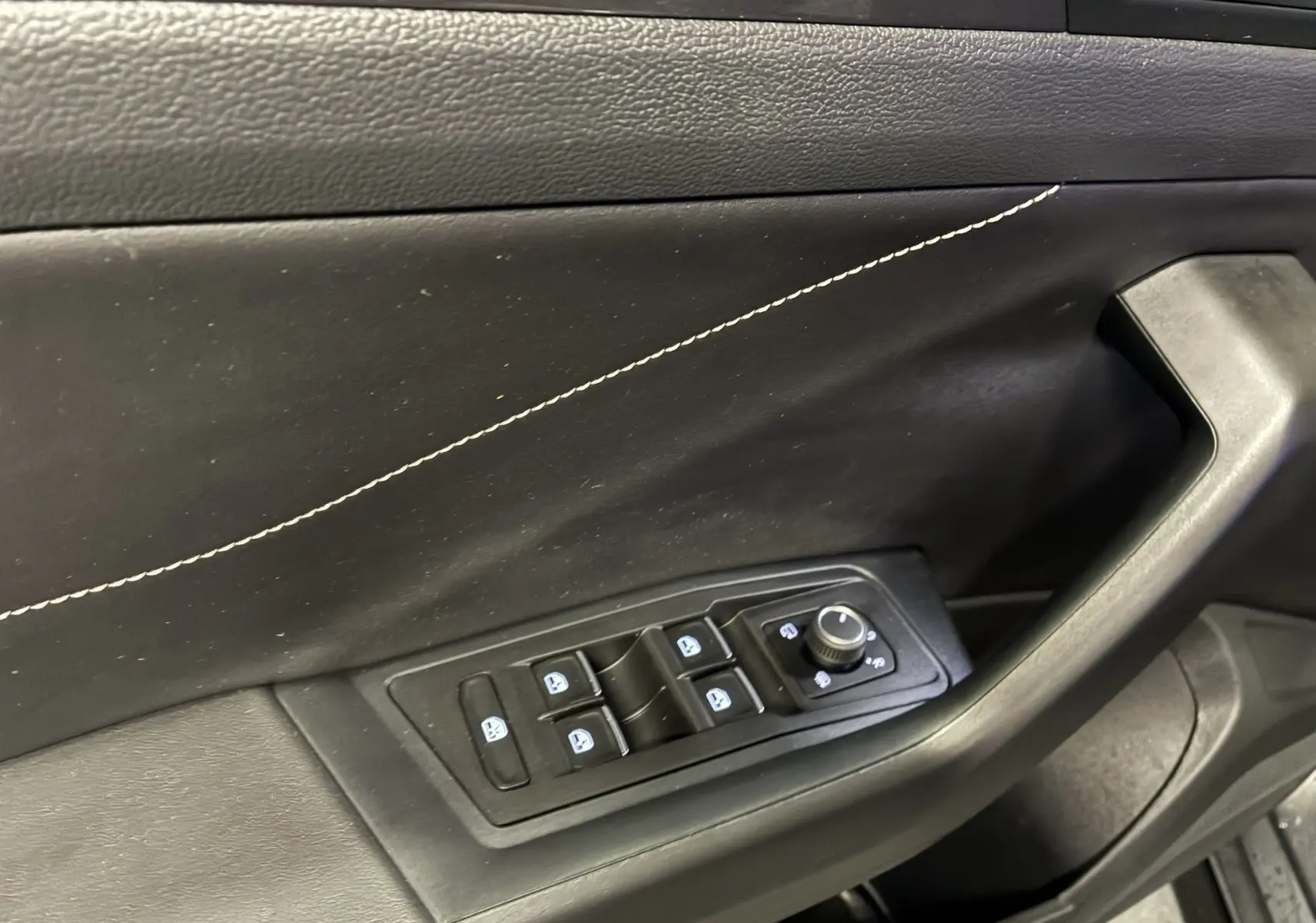 Détail de la porte intérieure côté conducteur du Volkswagen T-Roc gris, avec commandes électriques des vitres et réglage des rétroviseurs.