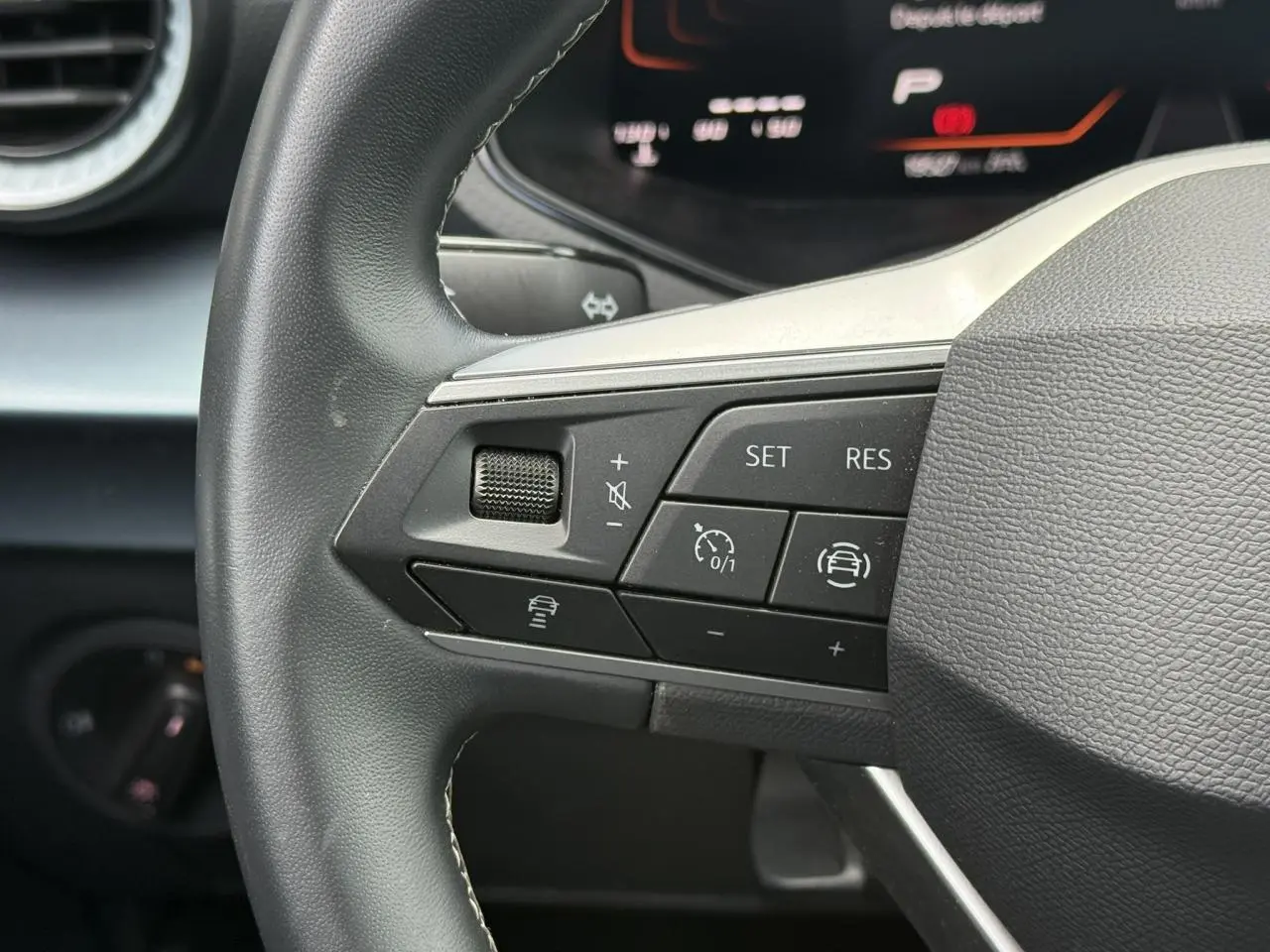 Gros plan sur les commandes de régulateur de vitesse au volant noir d’un SEAT Arona 2025, tableau de bord digital en arrière-plan.
