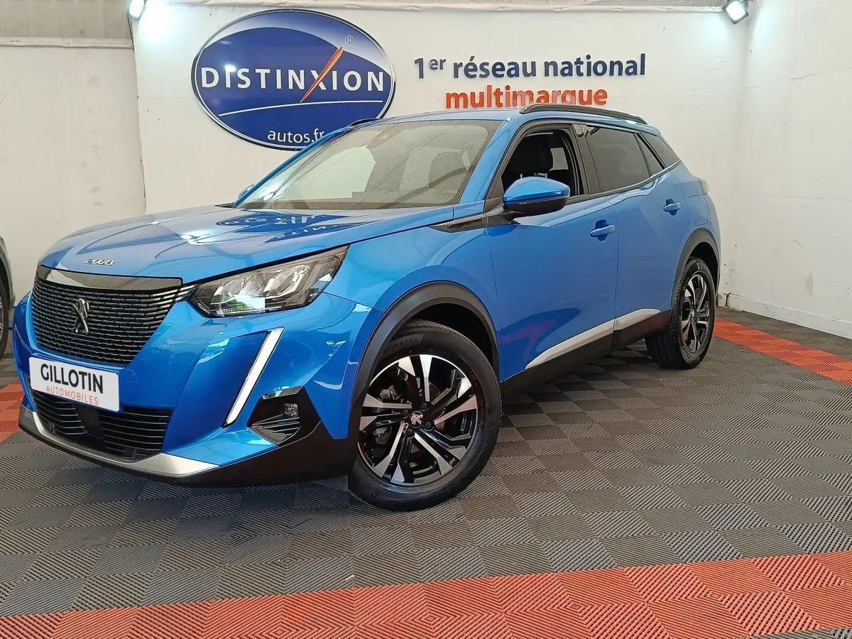 Peugeot 2008 bleu en 3/4 avant droit, avec calandre noire et jantes alliage bicolores visibles en intérieur showroom.