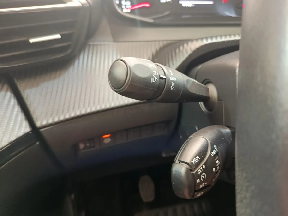 Gros plan sur les commandes de régulateur de vitesse et des phares à gauche du volant d’un Peugeot 2008 bleu 2021.