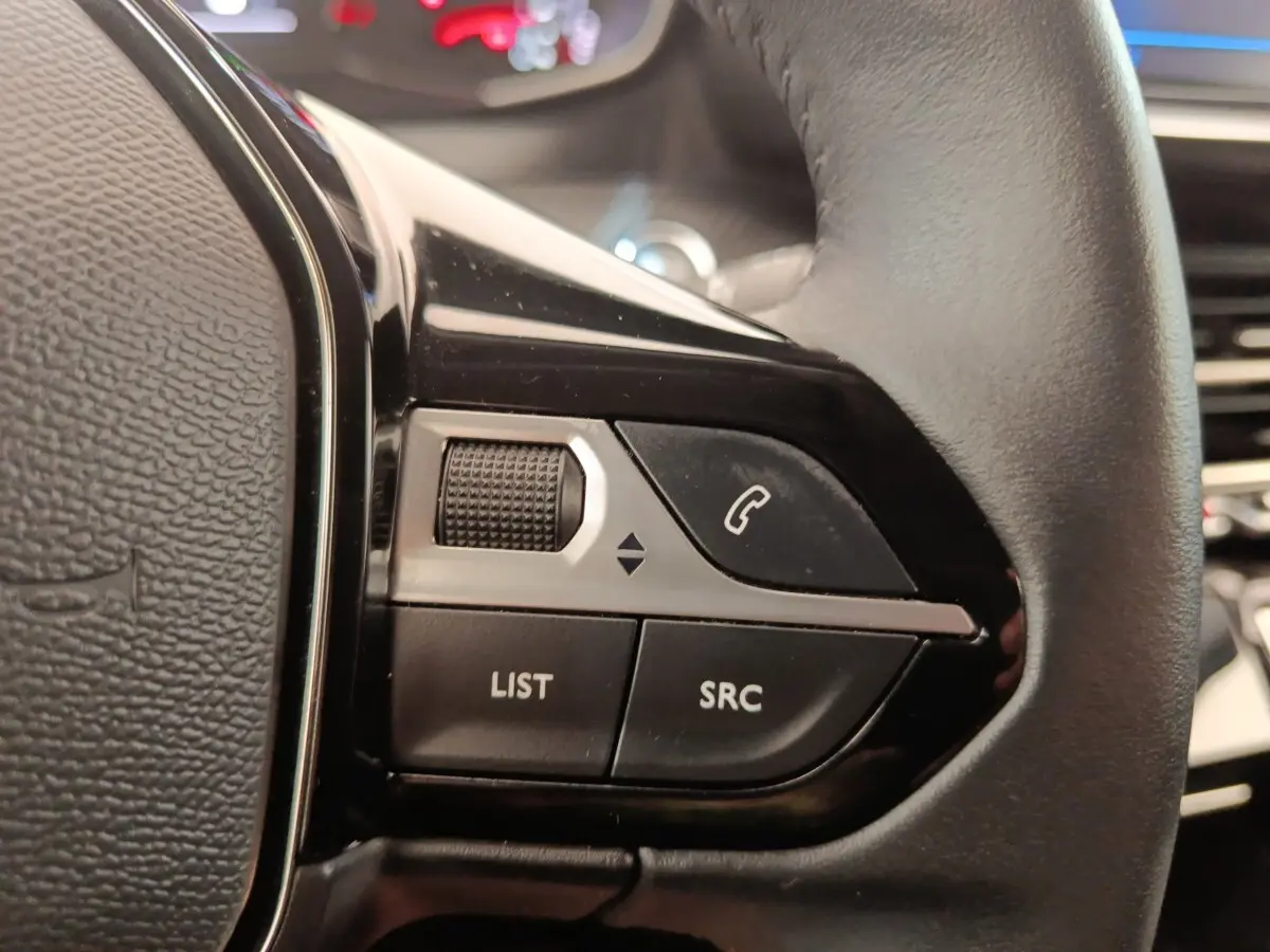 Gros plan sur les commandes multifonctions du volant cuir noir de la Peugeot 2008 PureTech 100 S&S Allure Pack.
