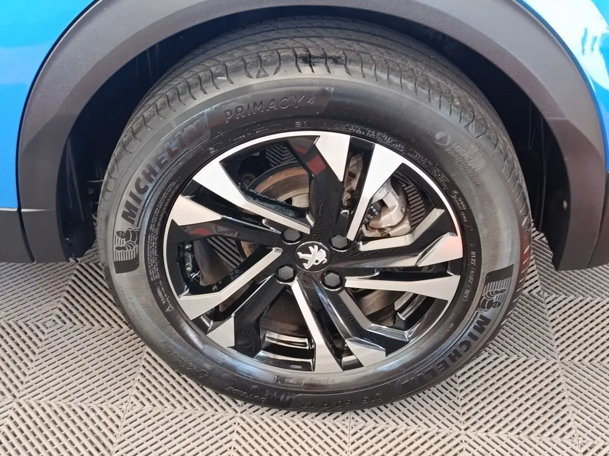 Gros plan sur la roue avant droite d’un Peugeot 2008 bleu avec jante alliage noire et argentée au design moderne.