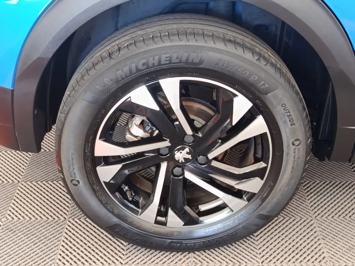Gros plan sur la roue avant gauche du Peugeot 2008 bleu, mettant en valeur la jante alliage noire et argentée avec logo Peugeot.