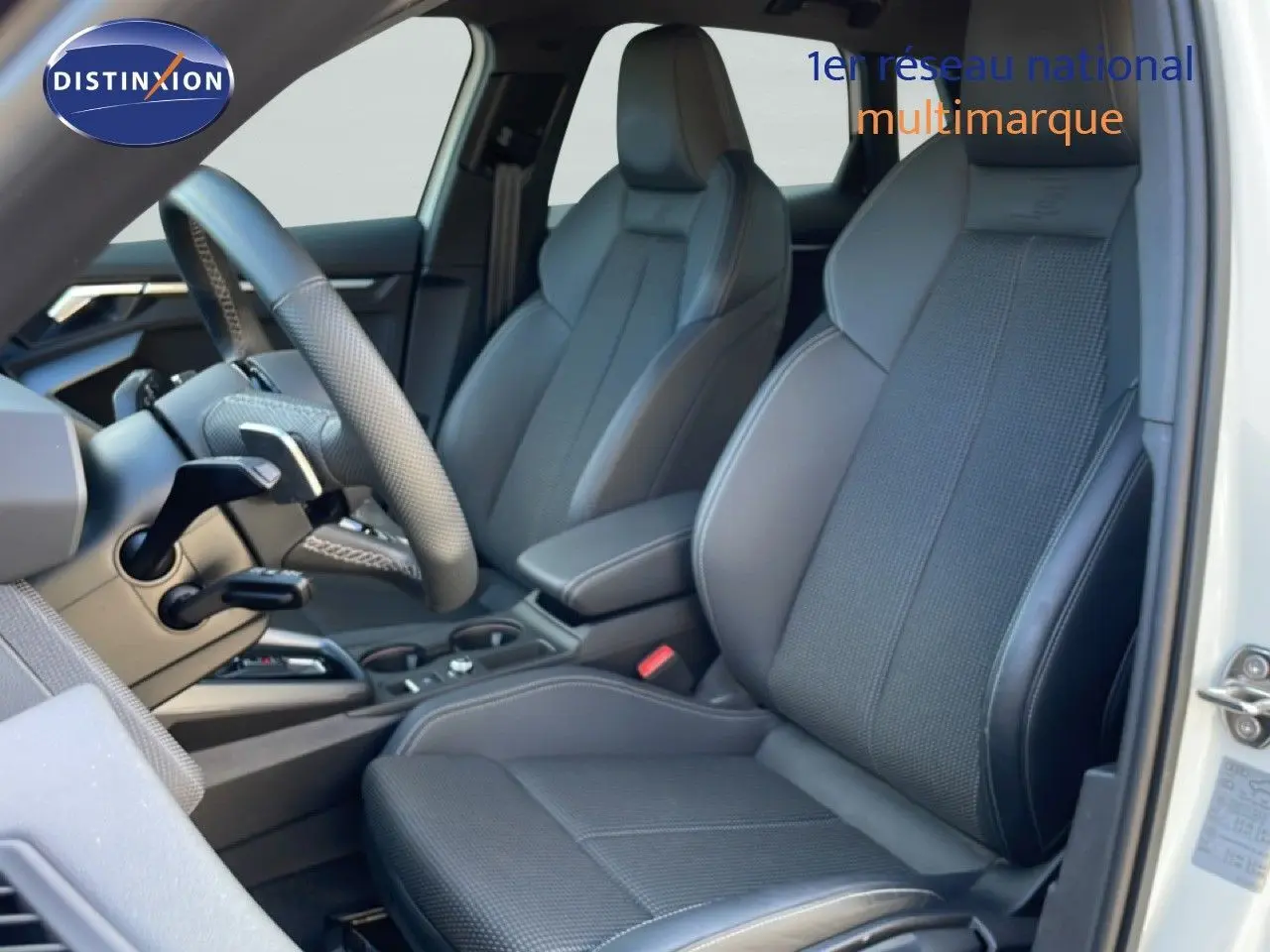 Vue intérieure côté conducteur de l'Audi A3 Sportback blanc Ibis, sièges sport gris noir avec volant cuir multifonction.