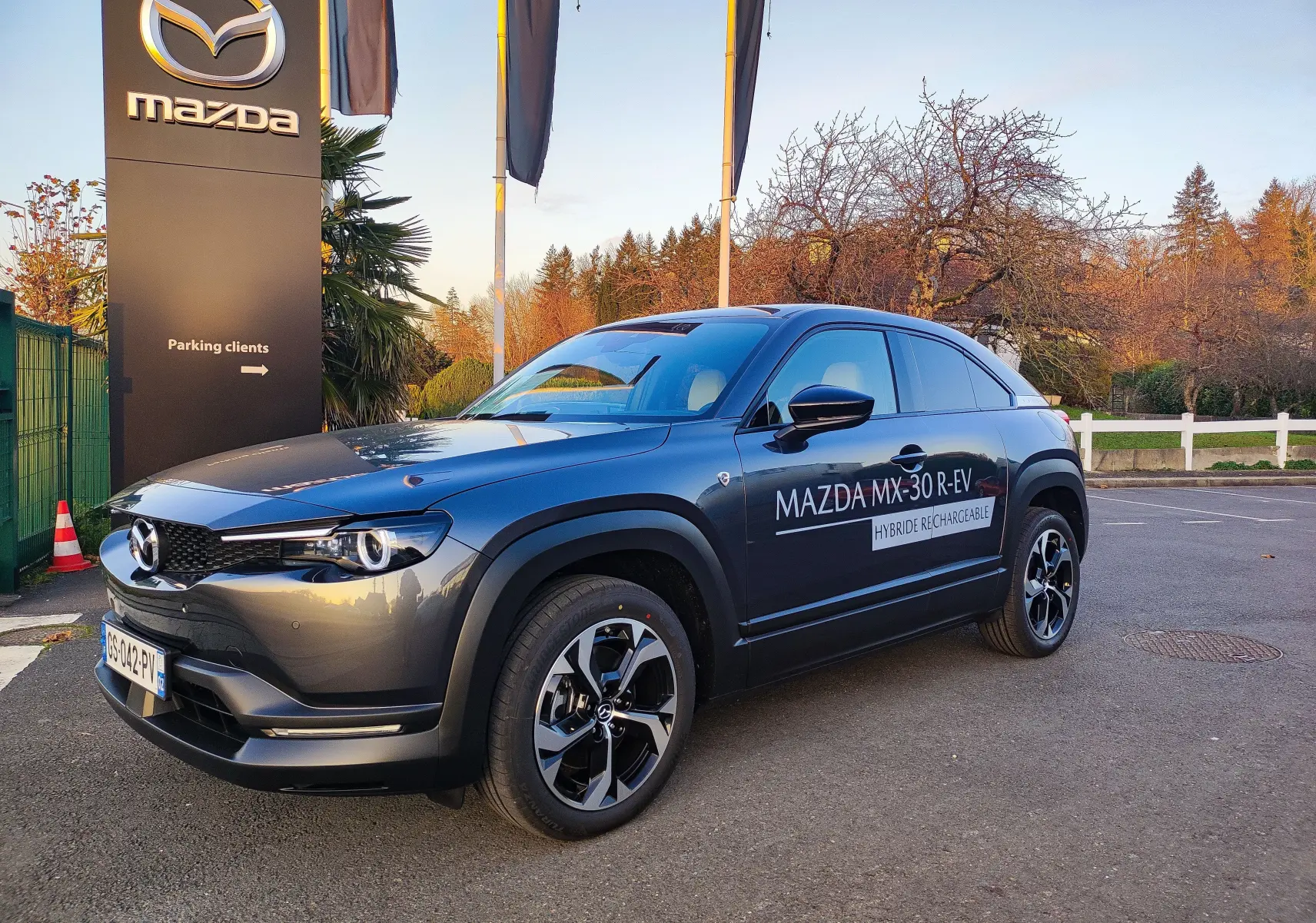 Vue 3/4 avant droite d'un Mazda MX-30 gris foncé hybride rechargeable avec logo et marquage sur la porte côté droit.