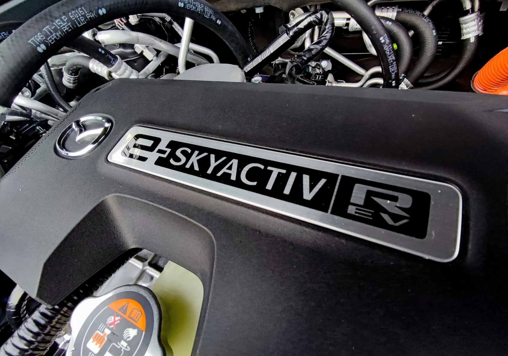 Gros plan sur le moteur e-SKYACTIV d'une Mazda MX-30 2023 hybride rechargeable, avec logo Mazda visible sur la couverture noire.