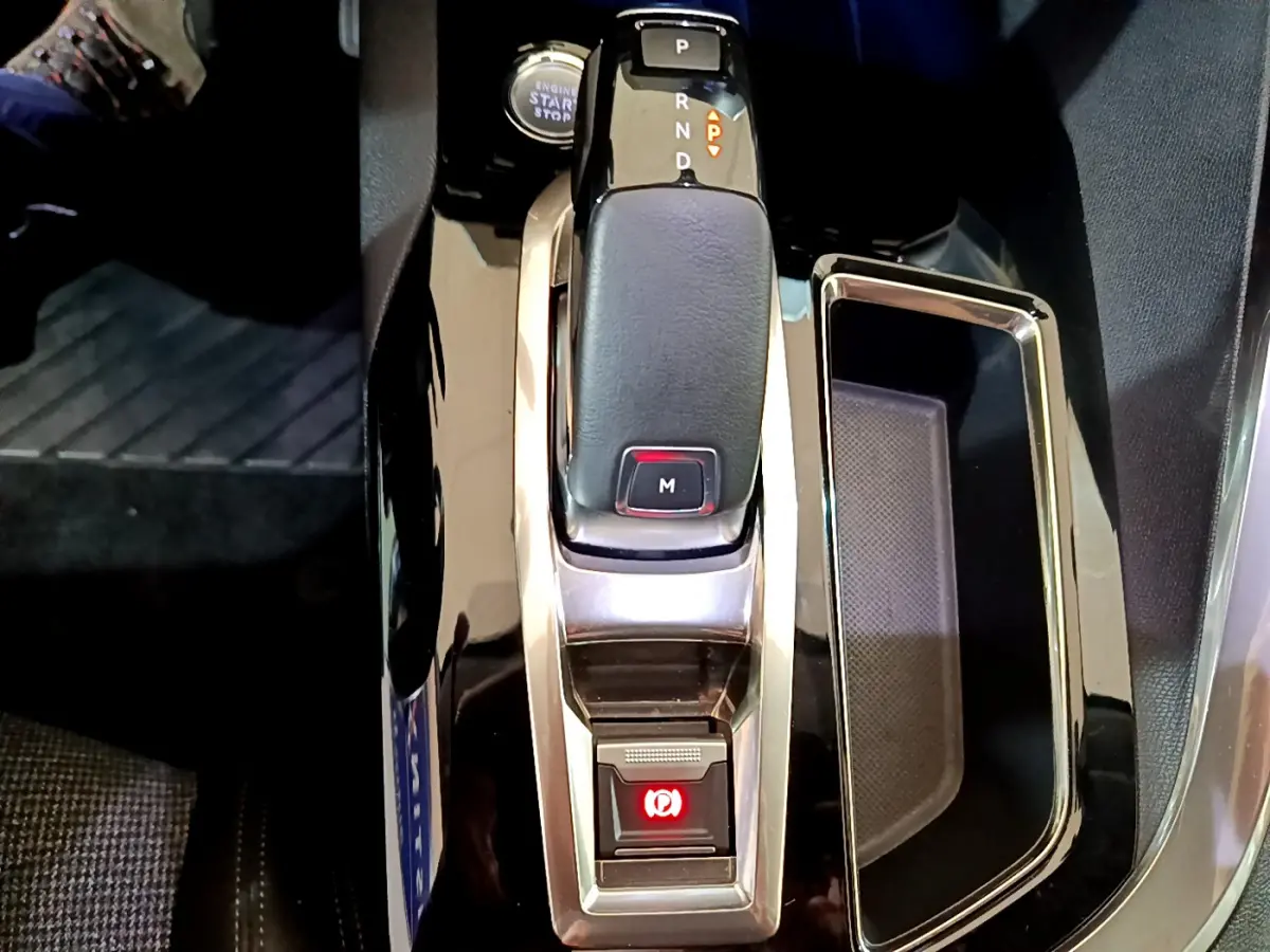 Gros plan sur la console centrale de la Peugeot 5008 gris clair, avec levier de vitesse automatique et frein à main électrique.