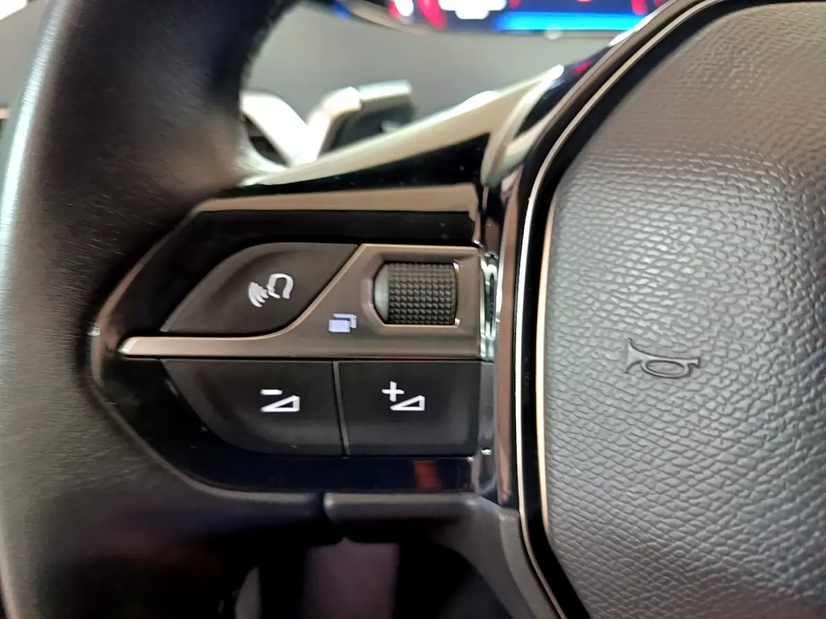 Gros plan sur les commandes gauche du volant cuir du Peugeot 5008 gris clair, avec boutons multifonctions et molette tactile.