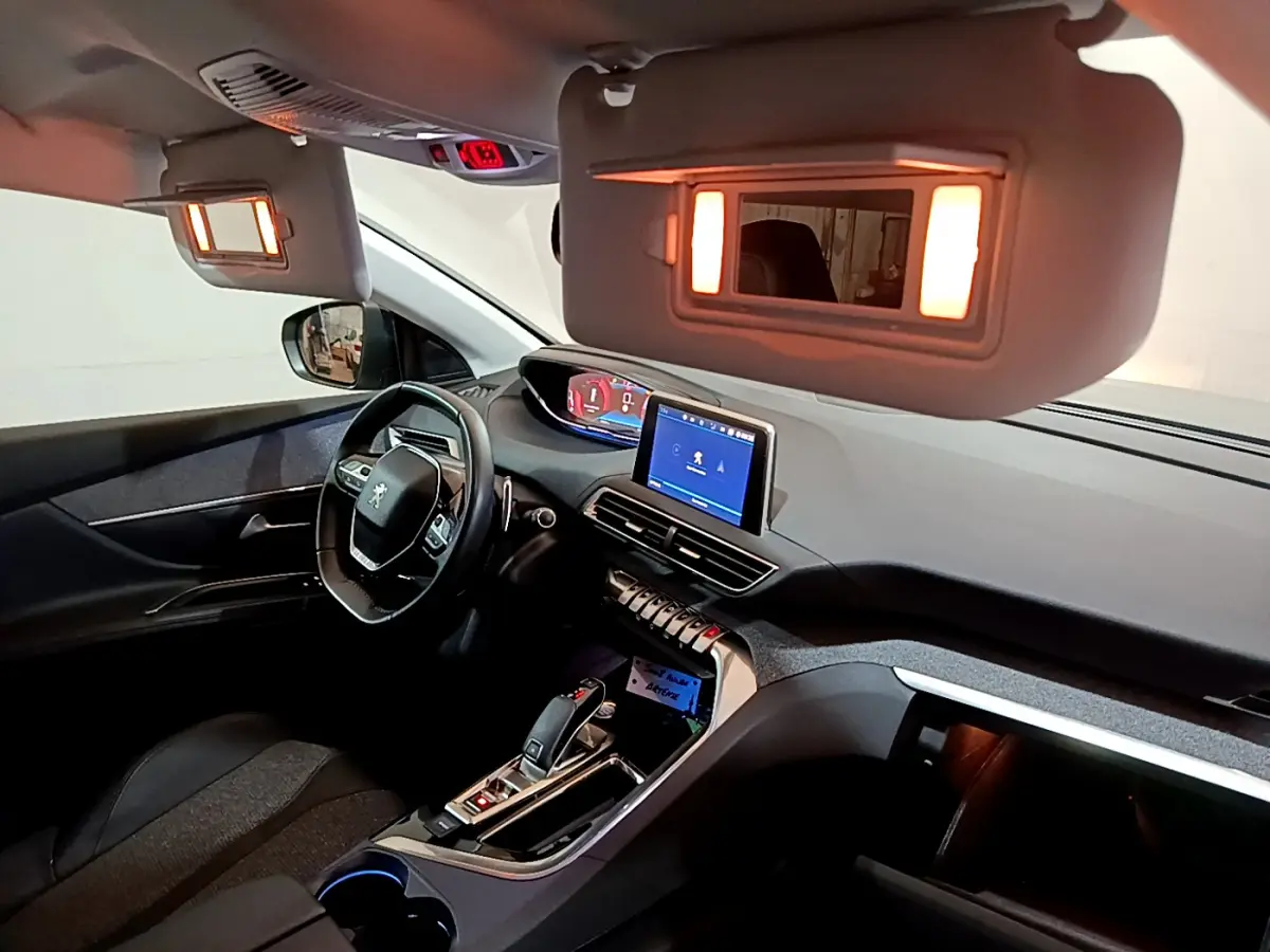 Intérieur du Peugeot 5008 gris clair vu côté conducteur, tableau de bord moderne avec écran tactile et miroir de soleil éclairé.