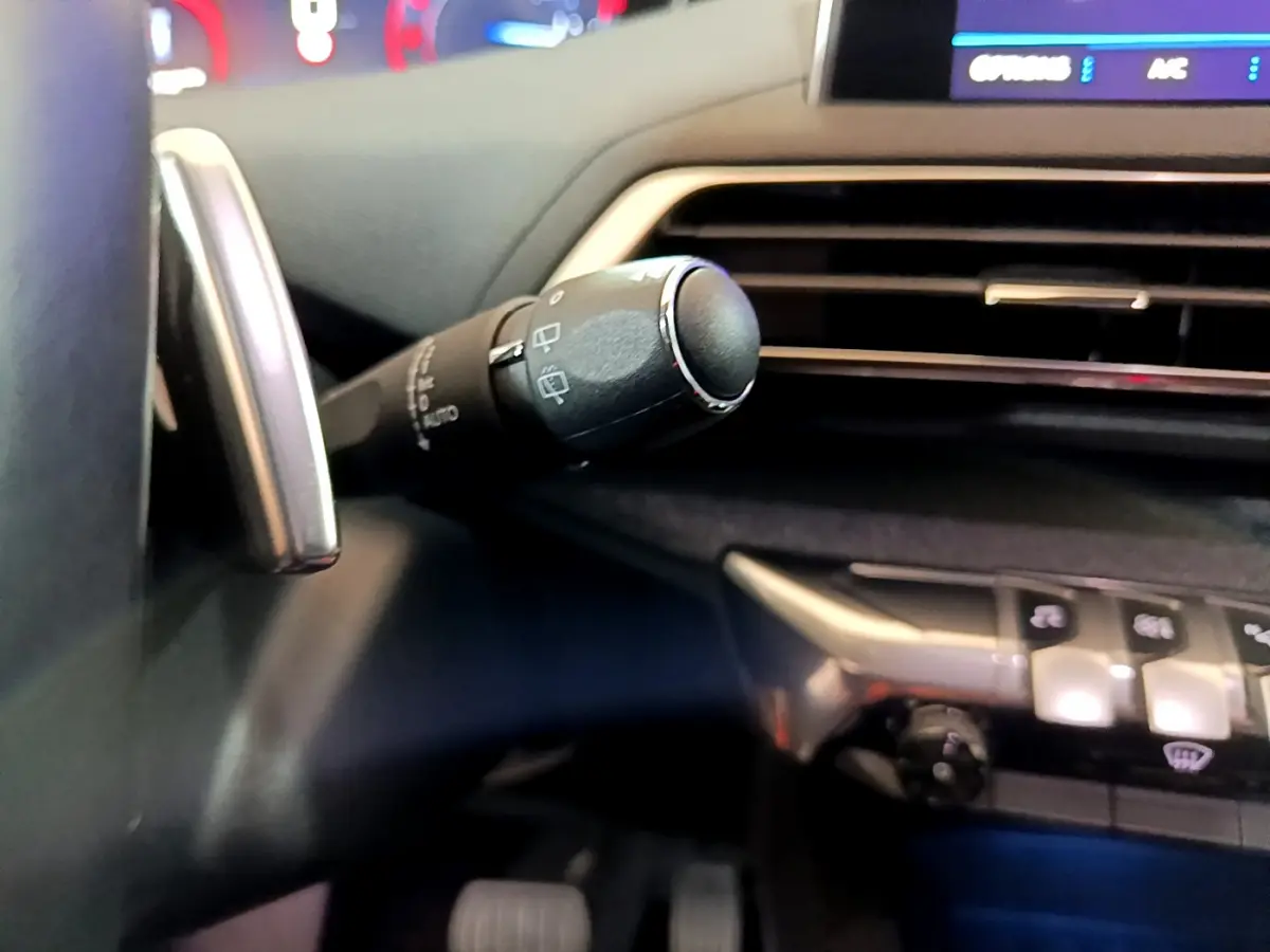 Gros plan sur la commande d'essuie-glace à gauche du volant dans l'habitacle sombre du Peugeot 5008 gris clair.