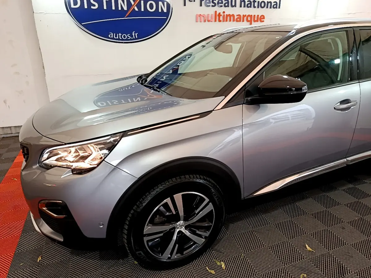 Vue 3/4 avant droit d'un Peugeot 5008 gris clair avec phares LED allumés et jantes alliage bicolores.