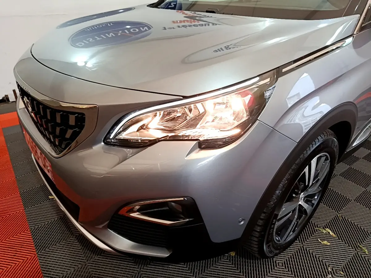 Vue 3/4 avant droit d'un Peugeot 5008 gris clair avec phares allumés et jantes alliage visibles.