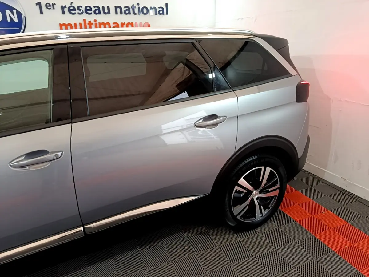 Vue côté droit arrière du Peugeot 5008 gris clair avec jante alliage et vitres teintées dans un showroom.