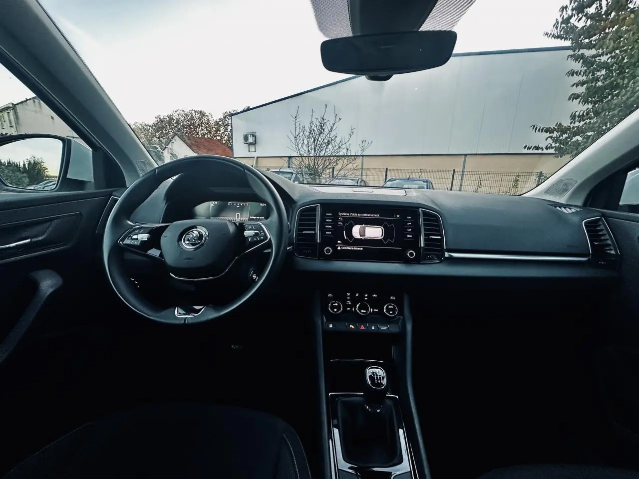Intérieur noir du Skoda Karoq 2024 vu de face, volant multifonctions et écran tactile affichant l'aide au stationnement.