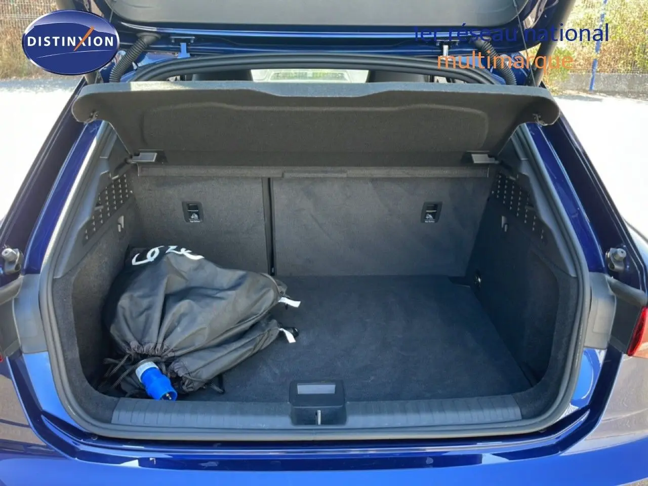 Coffre ouvert vu de l'arrière d'une Audi A3 Sportback bleu Navarre métal avec sac noir à l'intérieur.