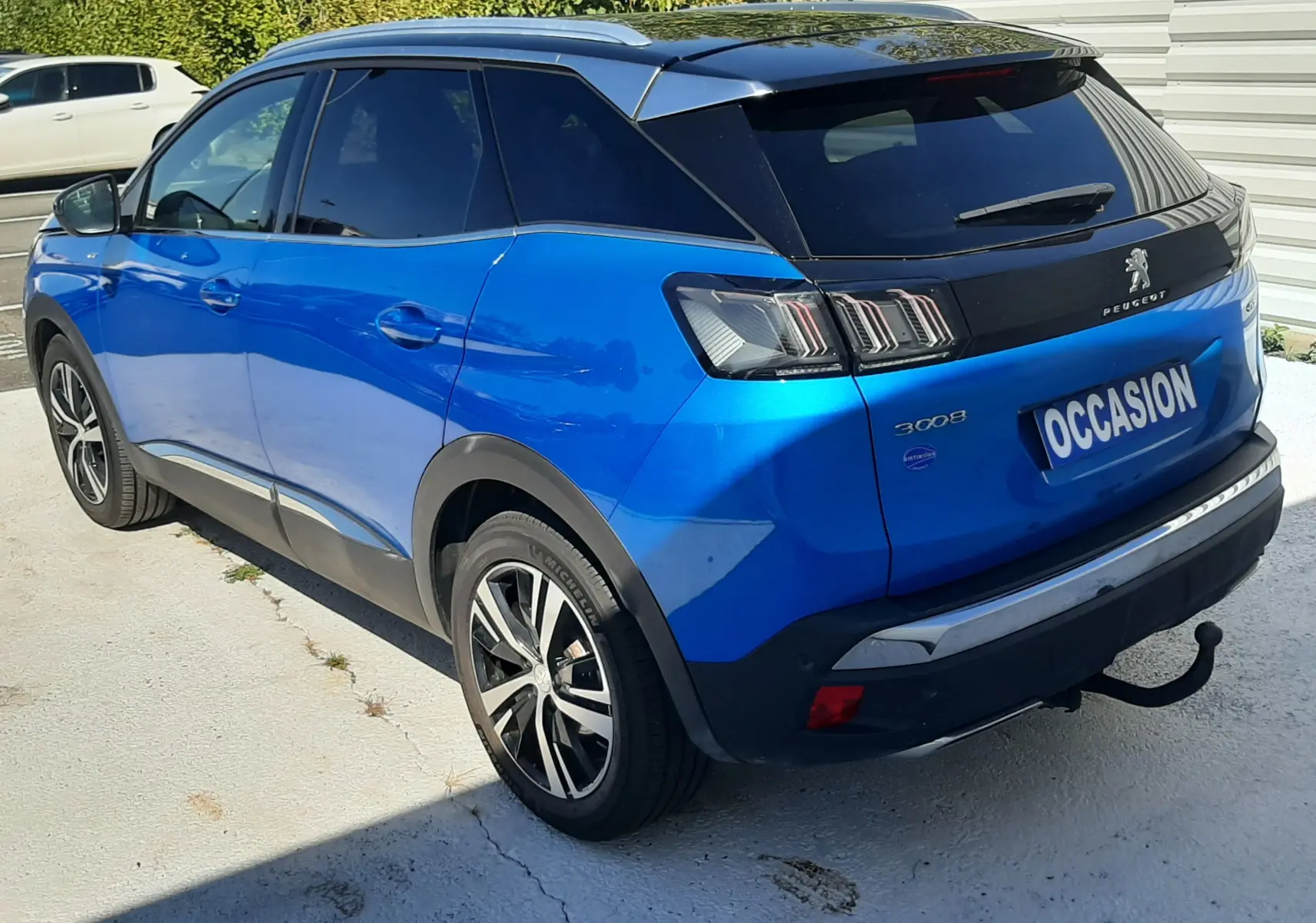 Peugeot 3008 bleu Vertigo vue 3/4 arrière droit avec toit noir Diamond et attelage visible sur parking extérieur.
