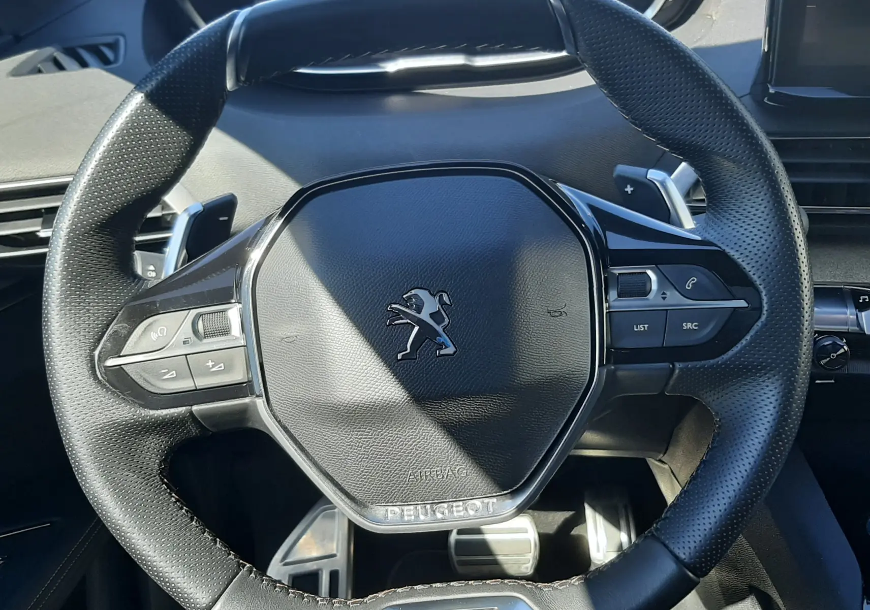 Vue rapprochée du volant cuir noir perforé du Peugeot 3008 GT avec logo lion et commandes intégrées.