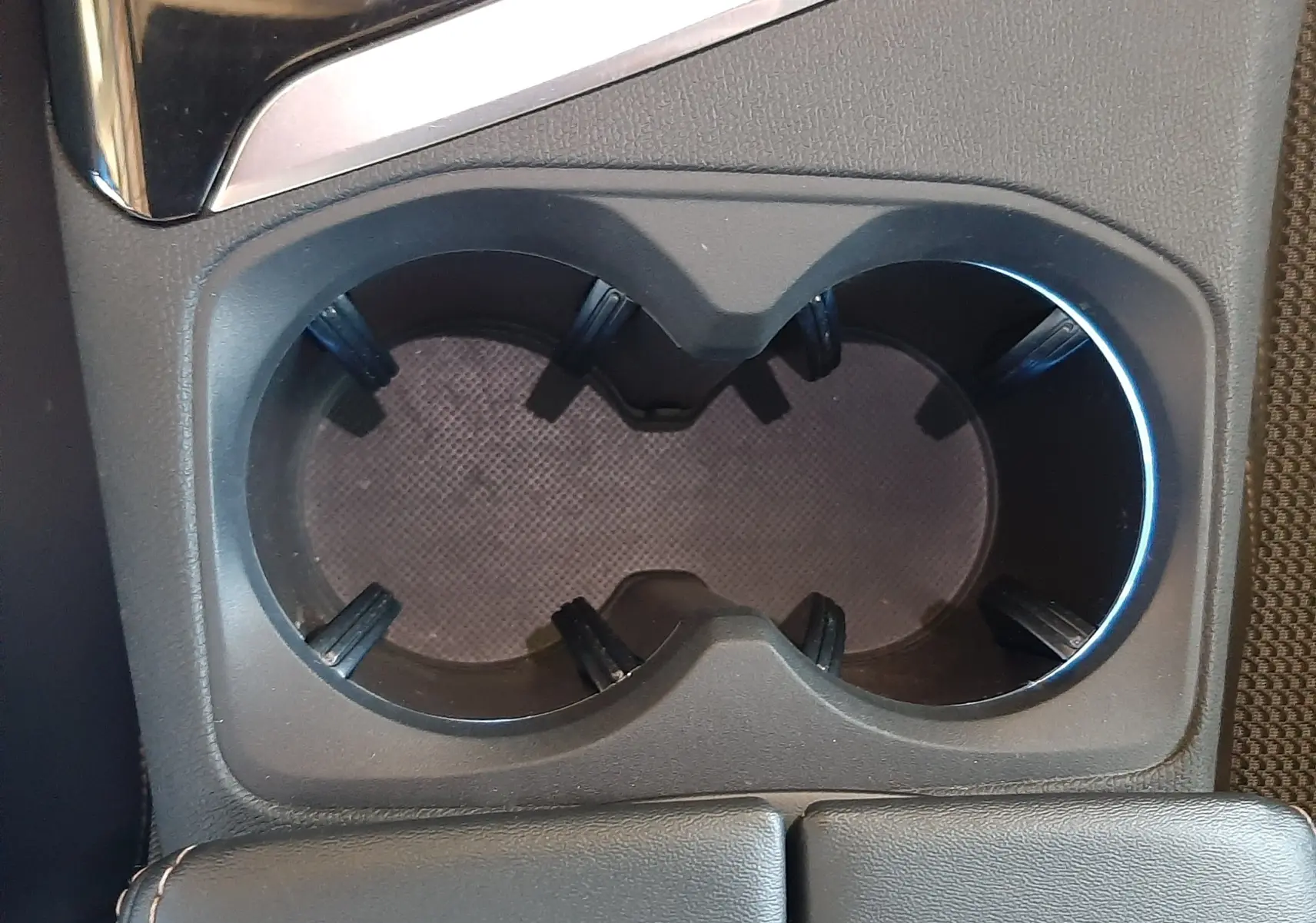 Gros plan sur les porte-gobelets centraux en plastique noir du Peugeot 3008 2023 avec accoudoir en cuir gris.
