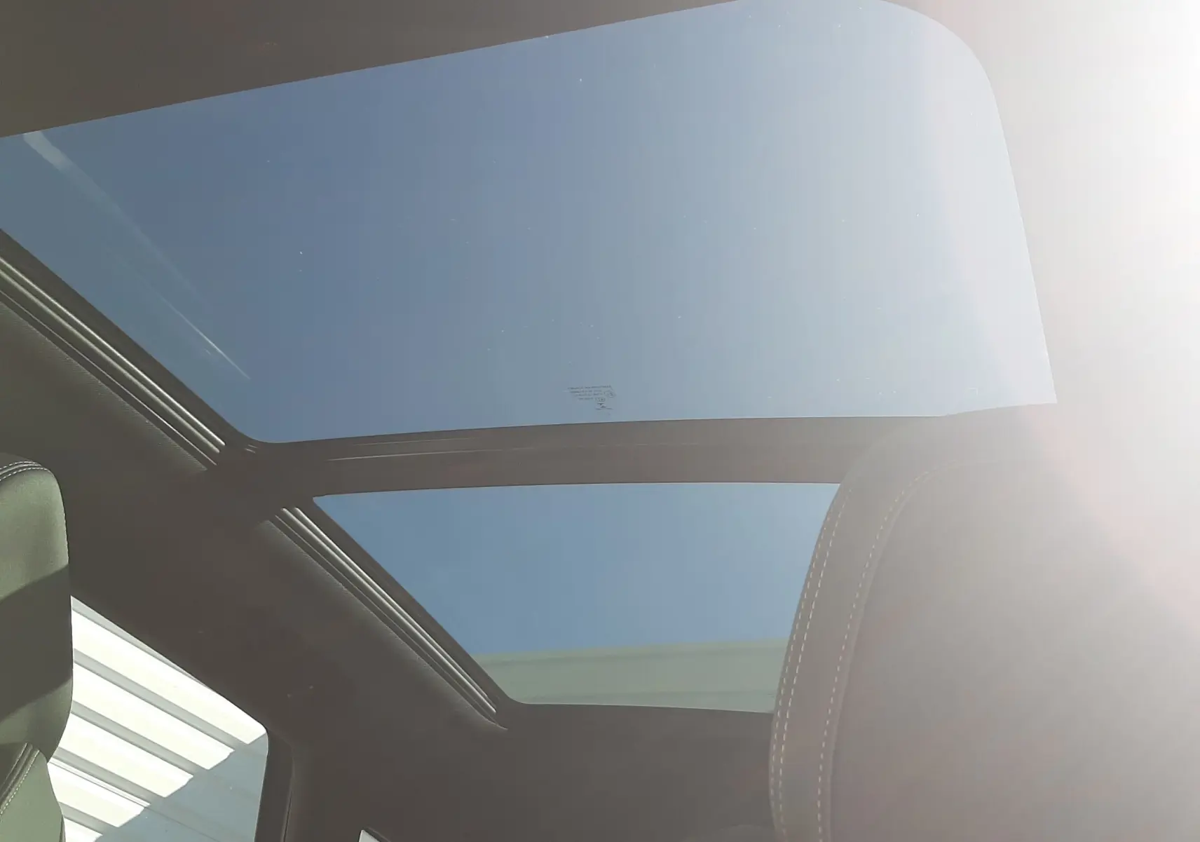 Vue intérieure du toit panoramique en verre du Peugeot 3008 GT 2023, avec ciel bleu visible et sièges noirs.