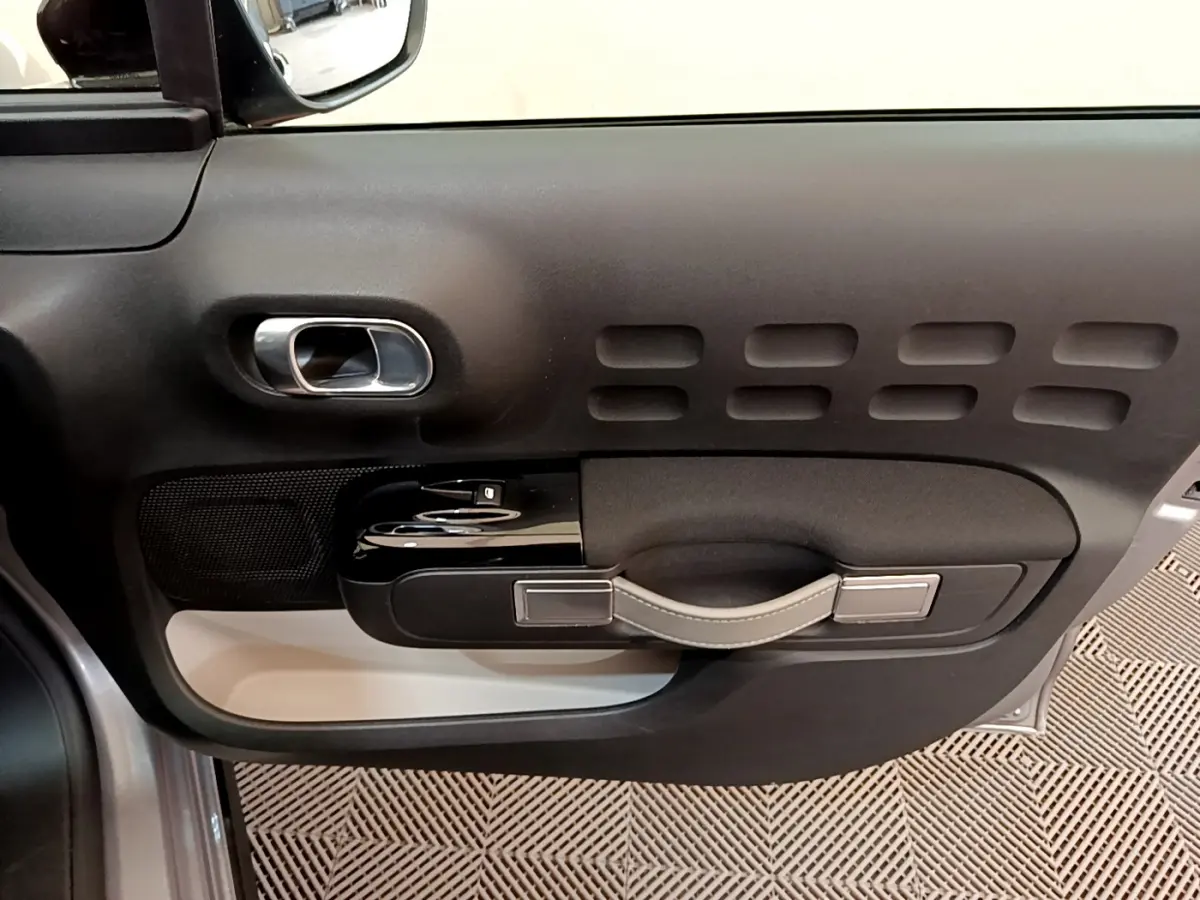 Vue rapprochée de la porte côté conducteur de la Citroën C3 gris clair, montrant la poignée et les commandes de fenêtre.