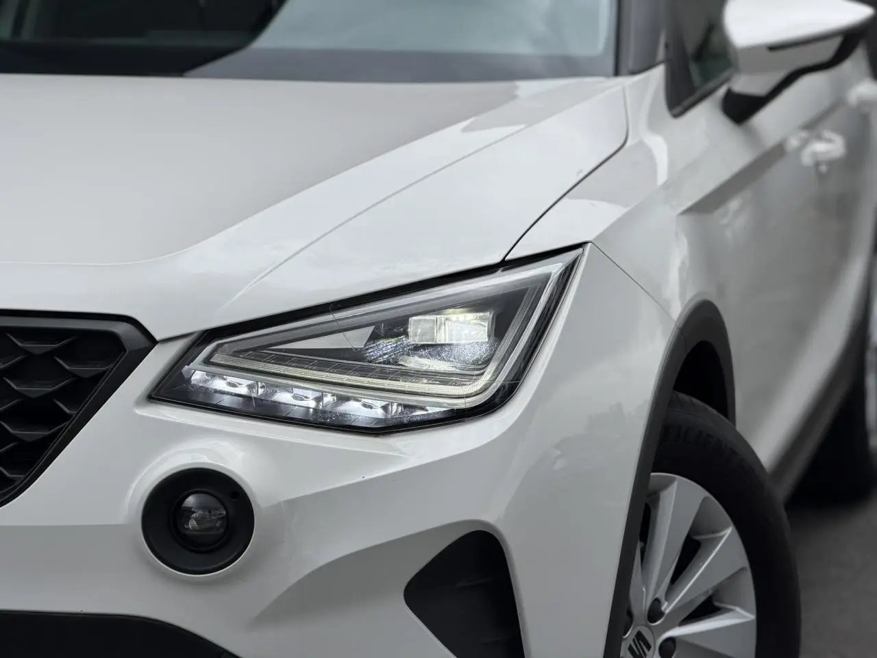 Gros plan sur l'avant droit blanc du SEAT Arona 2025, mettant en valeur le phare LED et la calandre noire.