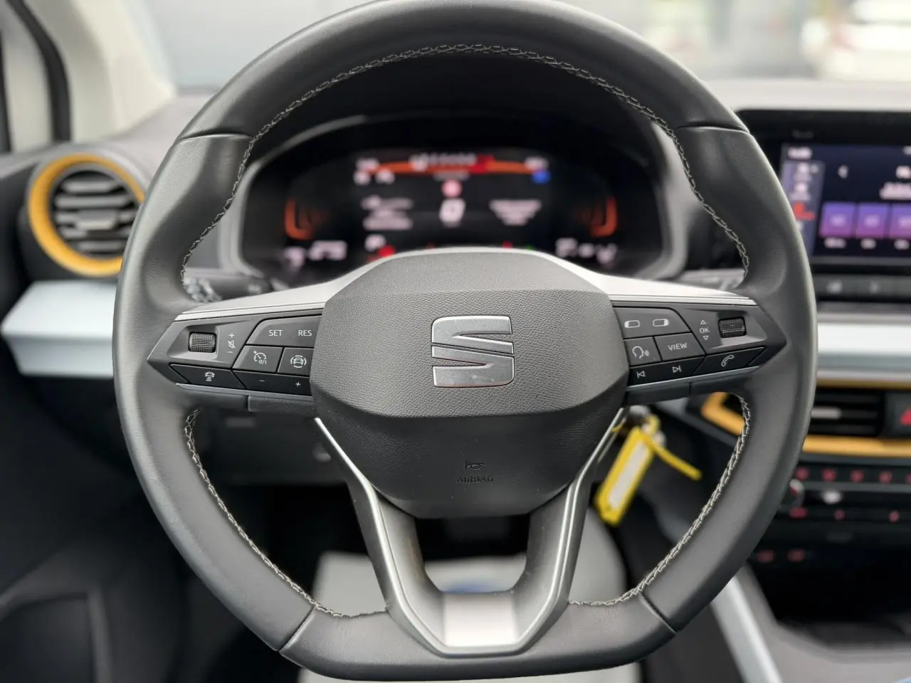 Vue rapprochée du volant noir du SEAT Arona 2025 avec commandes intégrées et tableau de bord digital flou en arrière-plan.