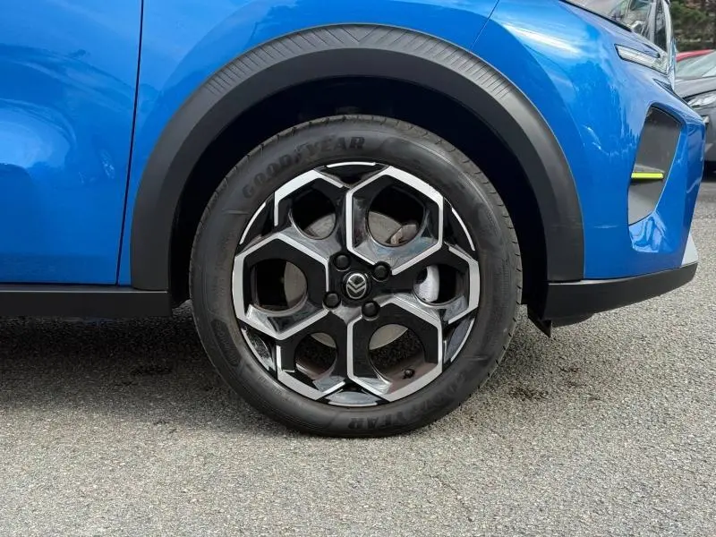 Gros plan sur la roue avant droite d'une Citroën C3 bleue, mettant en valeur la jante noire et argent au design hexagonal.