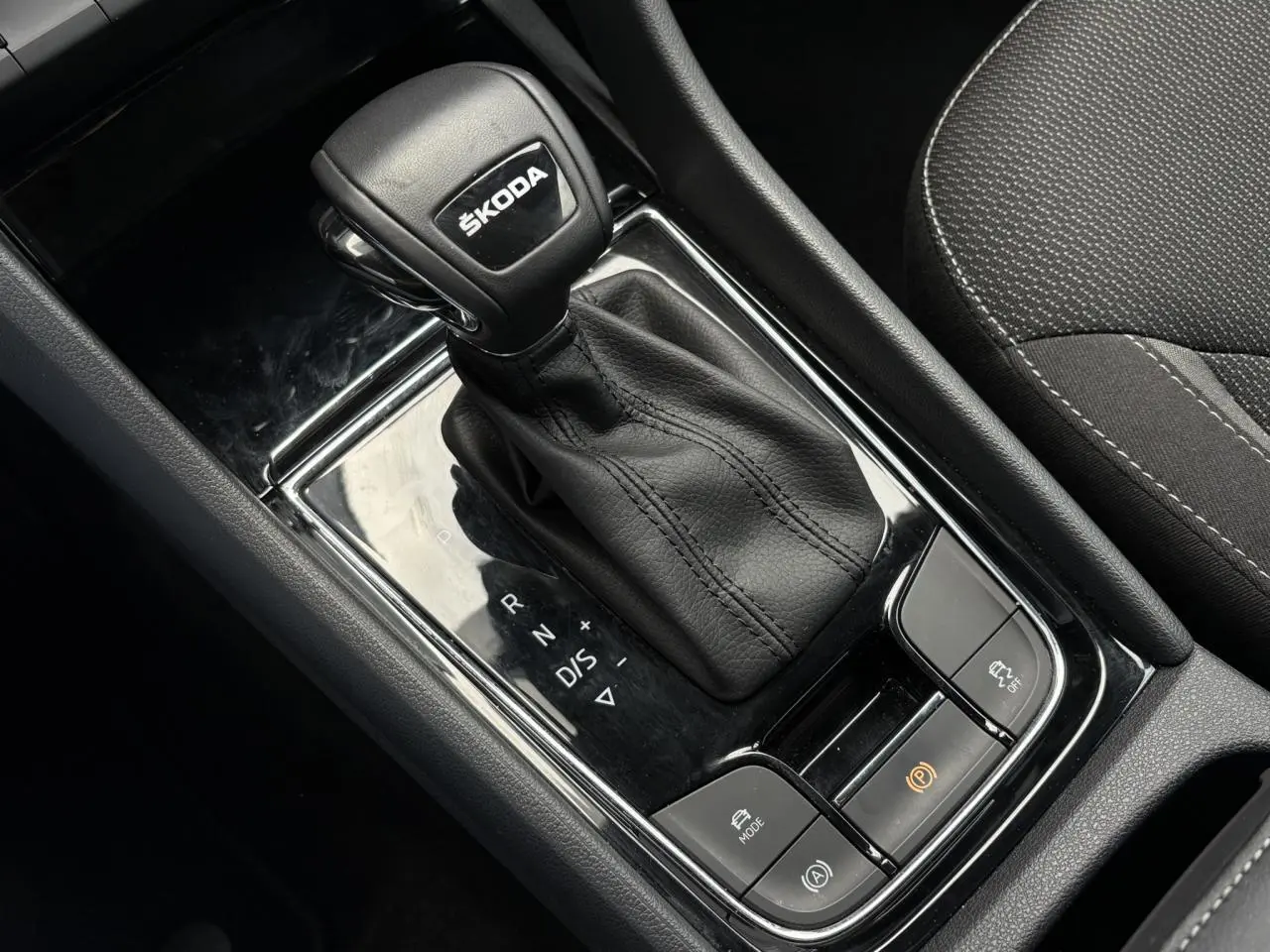 Le levier de vitesses automatique noir avec logo ŠKODA, entouré de commandes, intérieur tissu gris du ŠKODA KODIAQ 2024.