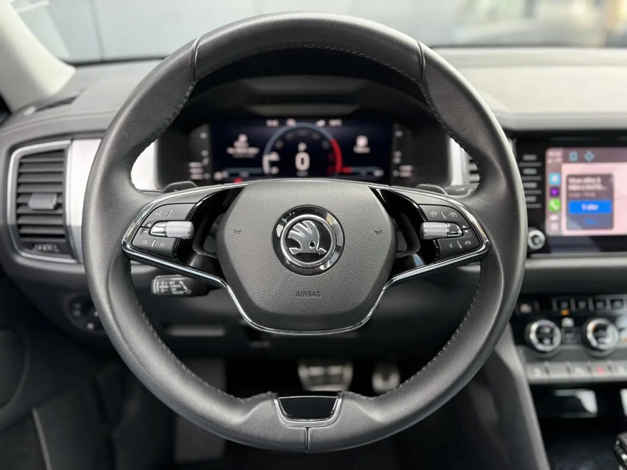 Volant cuir noir avec logo Skoda au centre, tableau de bord numérique et écran tactile du Skoda Kodiaq 2024 visible en arrière-plan.