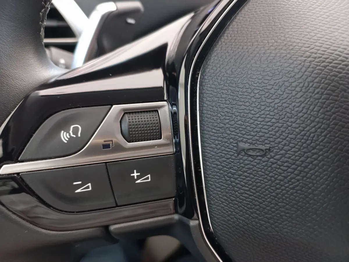Gros plan sur les commandes vocales et volume du volant cuir noir du Peugeot 5008 gris foncé, version 2021 Allure Pack.