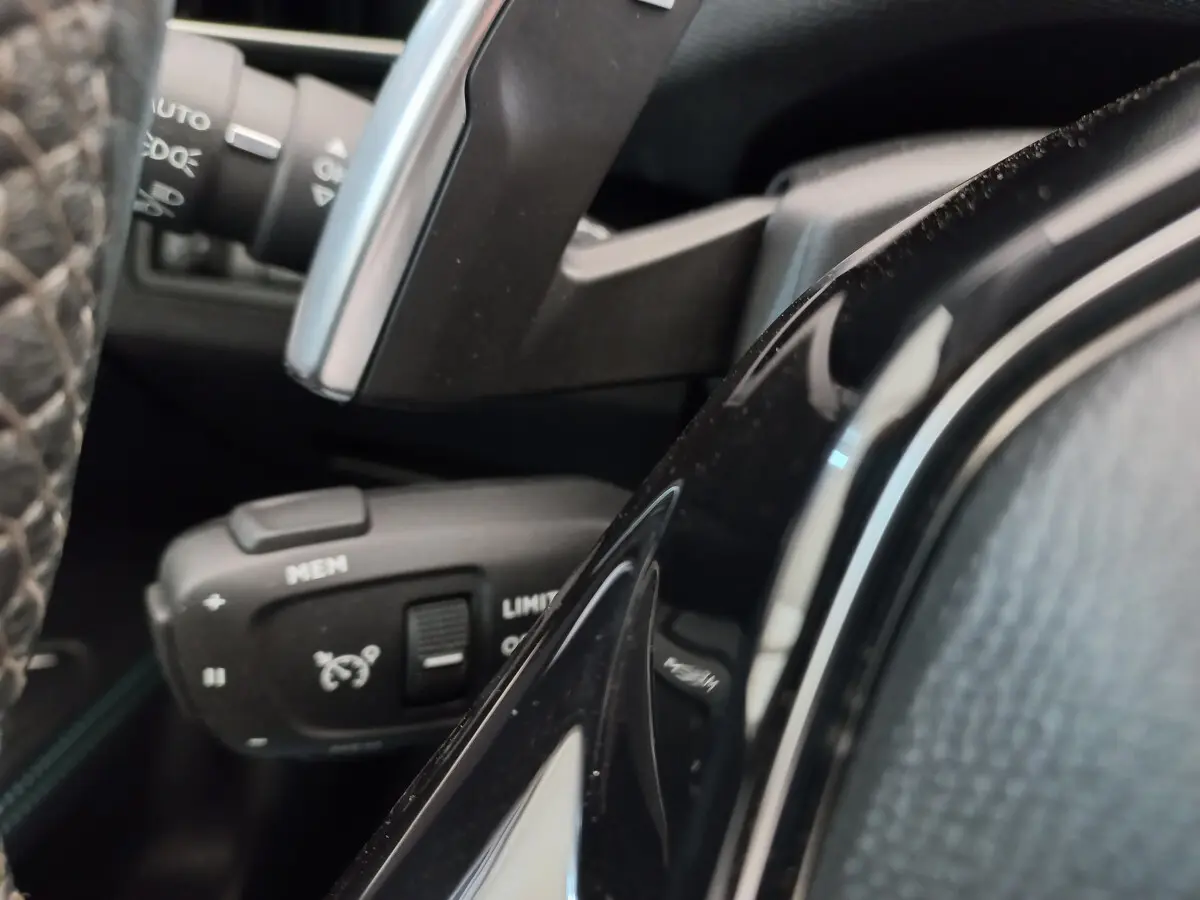 Gros plan sur la commande de régulateur de vitesse et limiteur, volant cuir noir du Peugeot 5008 gris foncé.