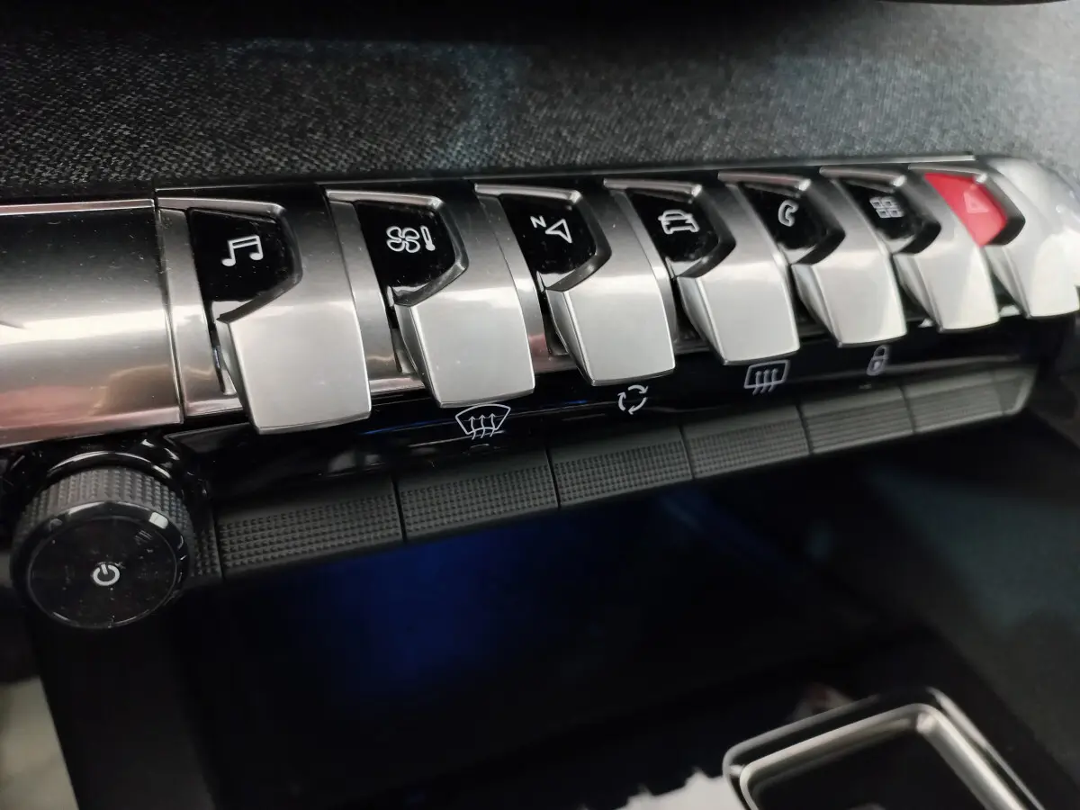 Gros plan sur les commandes chromées du tableau de bord du Peugeot 5008 2021, boutons multifonctions alignés.
