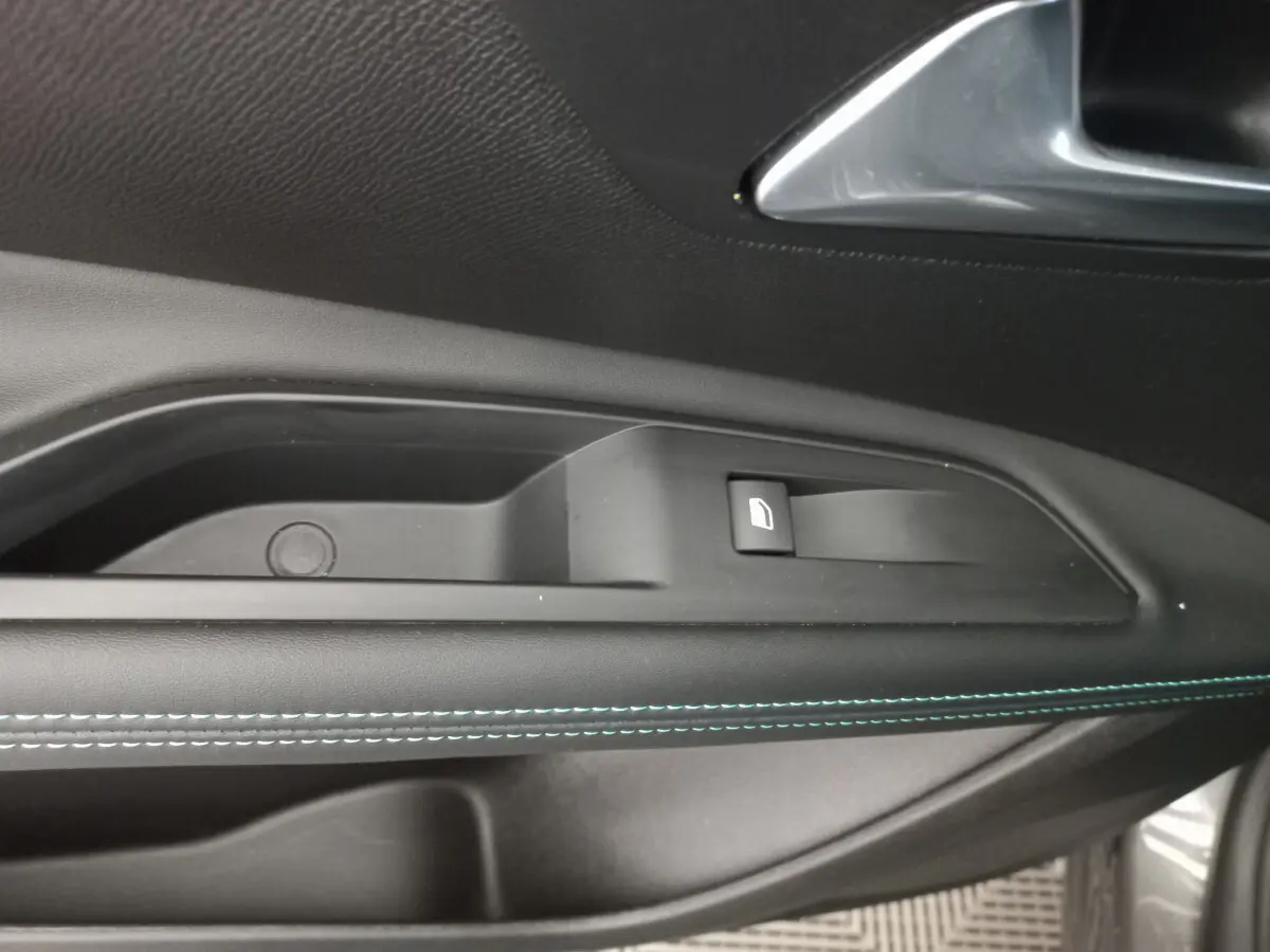 Gros plan sur la poignée intérieure côté gauche de la porte d’un Peugeot 5008 gris foncé avec surpiqûres bleues.