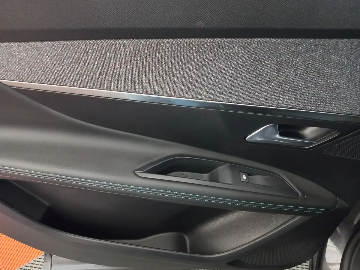 Gros plan sur la porte intérieure côté gauche du Peugeot 5008 gris foncé, avec poignée et bouton de vitre électrique.